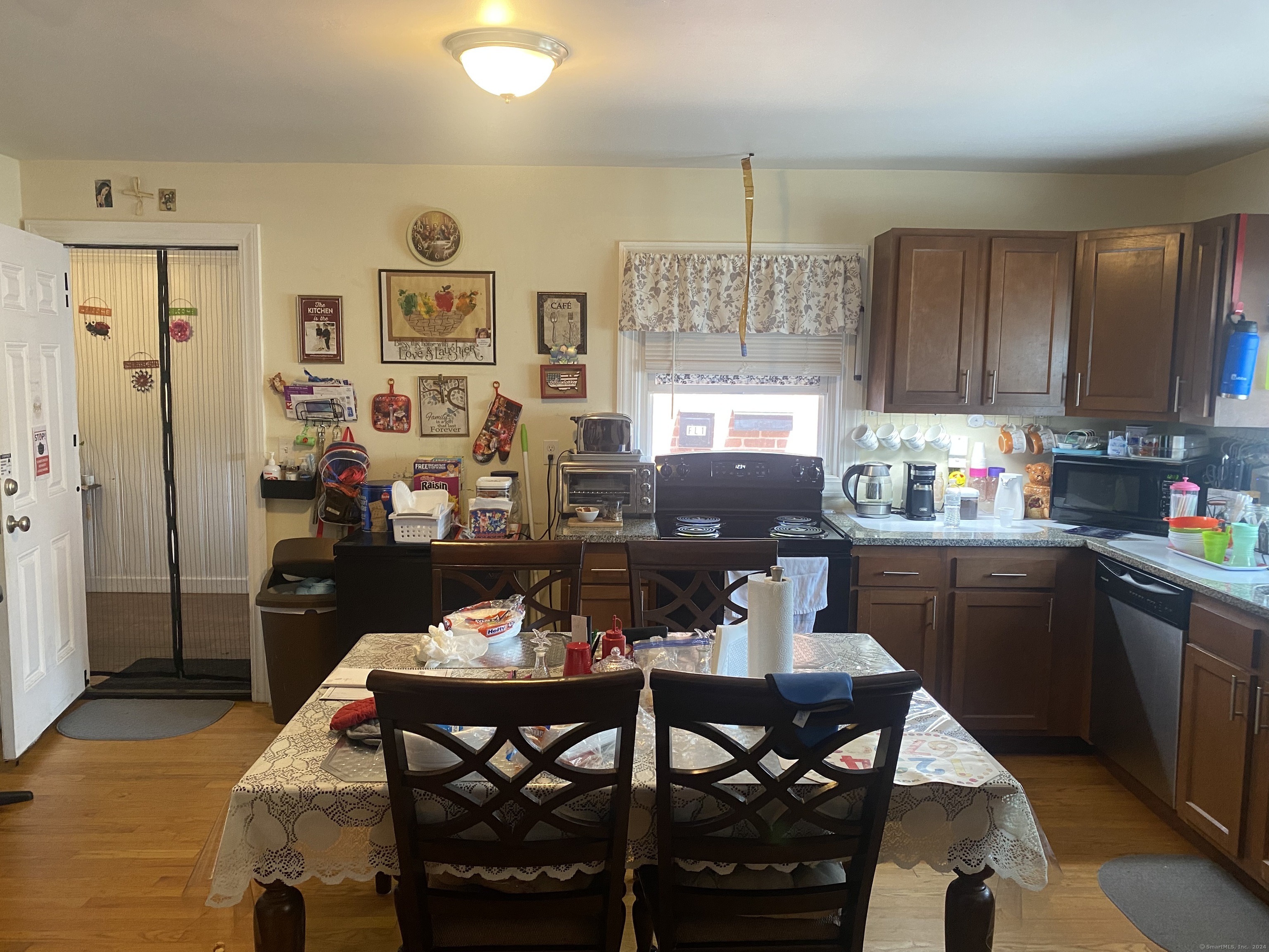 Kitchen and dining area with dark wood cabinets, a window above the stove, and a lace-covered table.