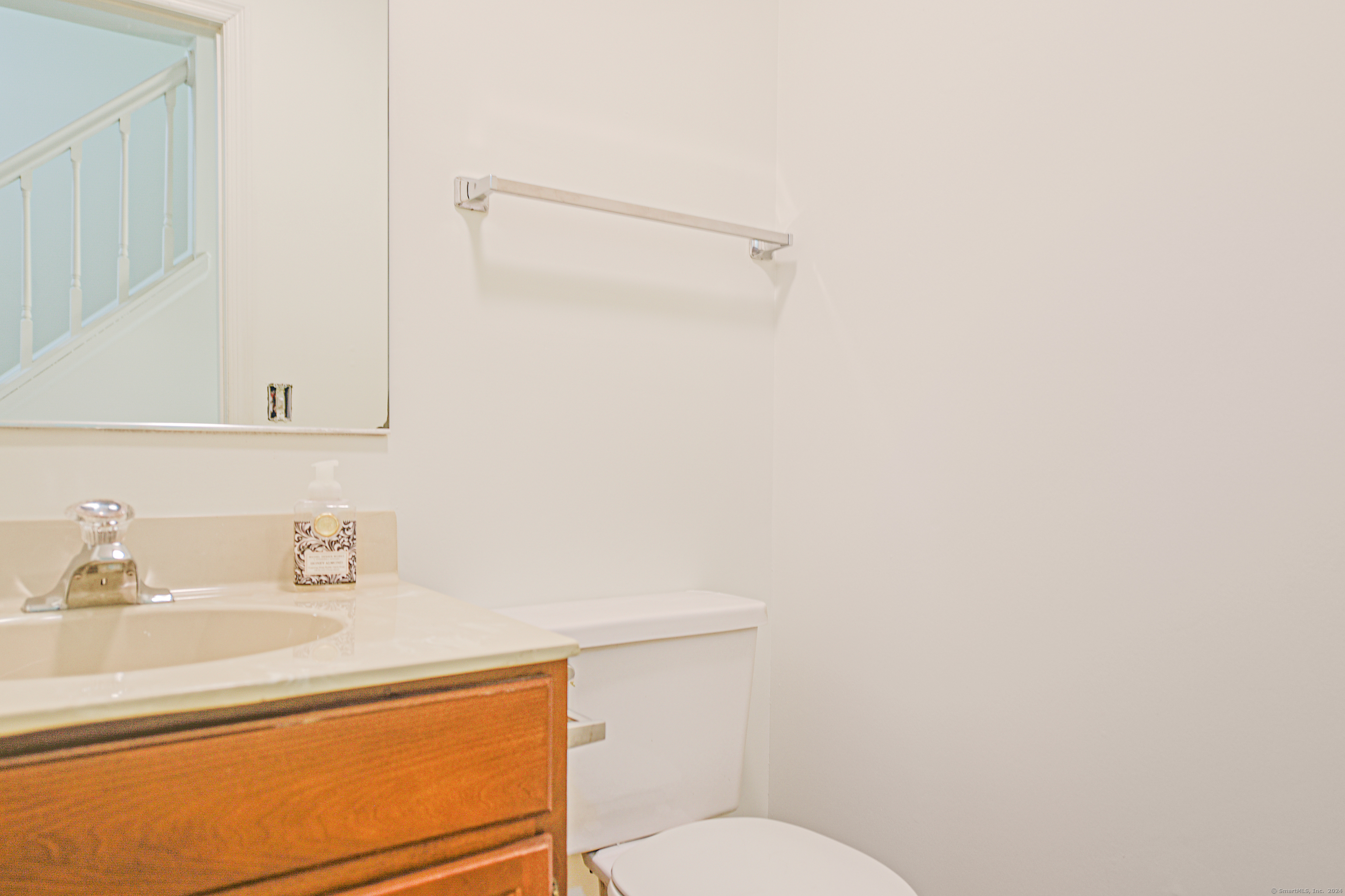 Bathroom with a wood vanity, cream countertop, white toilet, and wall mirror.
