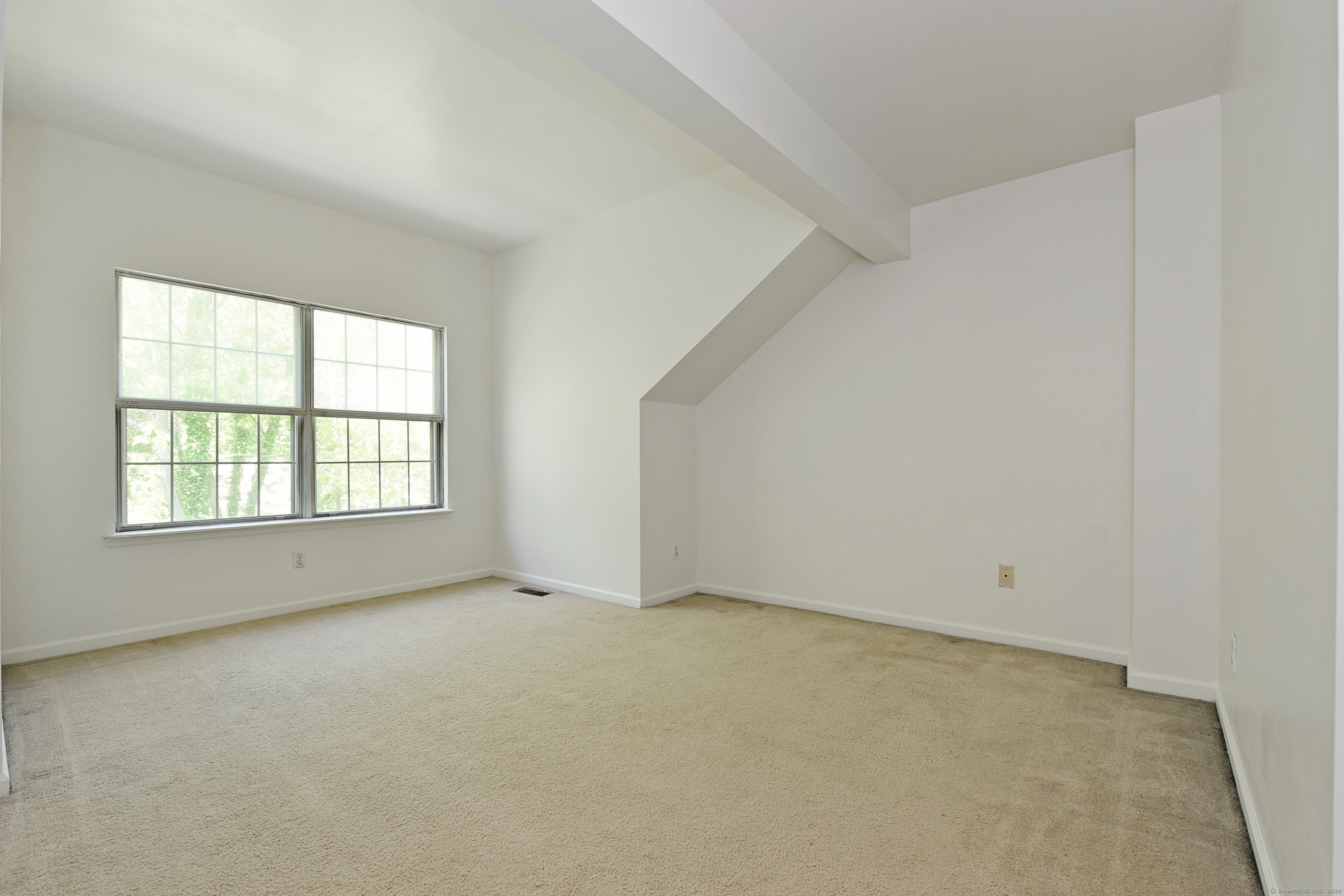Empty carpeted bedroom with a sloped ceiling and a large window overlooking trees.