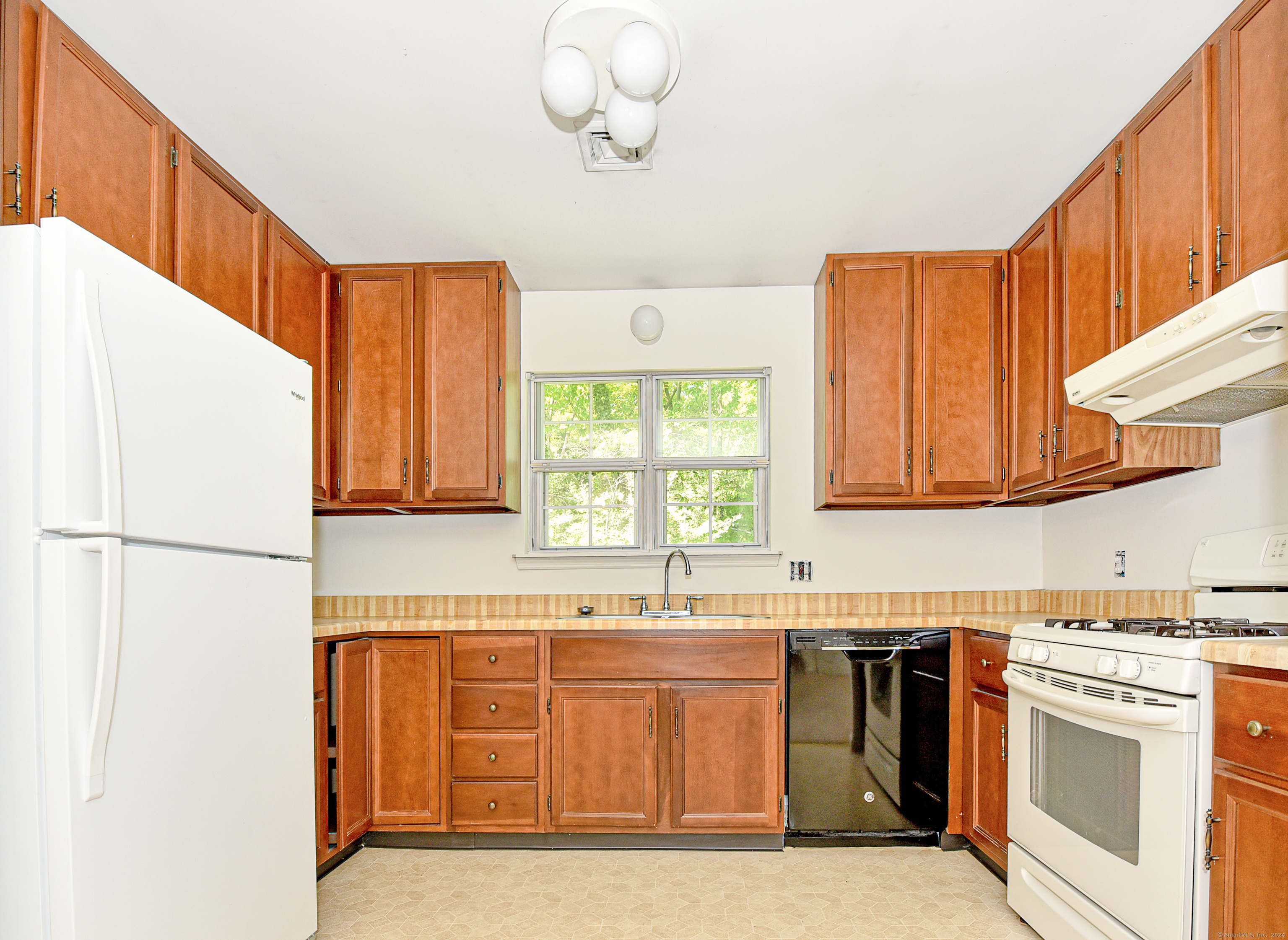 Kitchen with reddish-brown wood cabinets, a window above the sink, and white appliances.