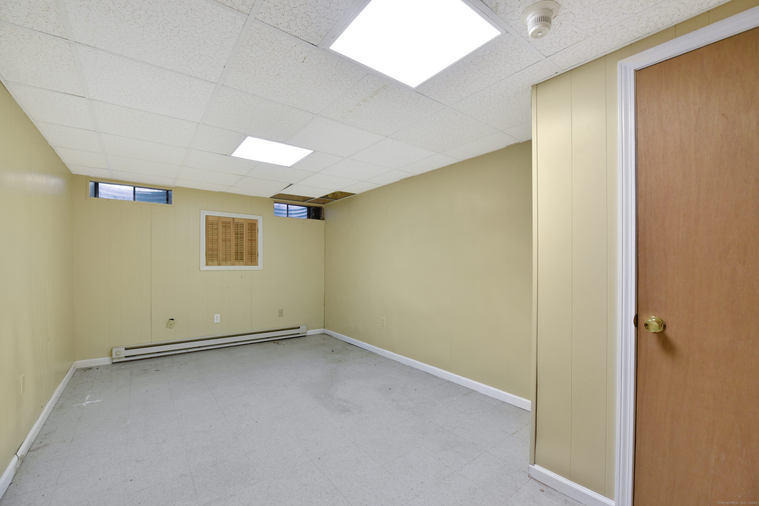 Vacant room with pale yellow walls, gray tile floor, baseboard heater, and missing ceiling panels.