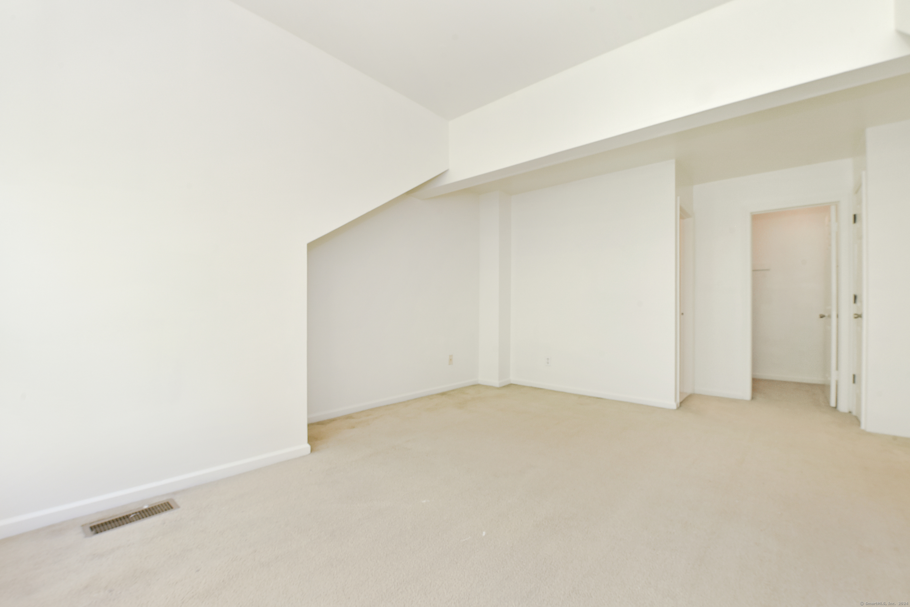 Empty carpeted room with a sloped ceiling and open doorways.