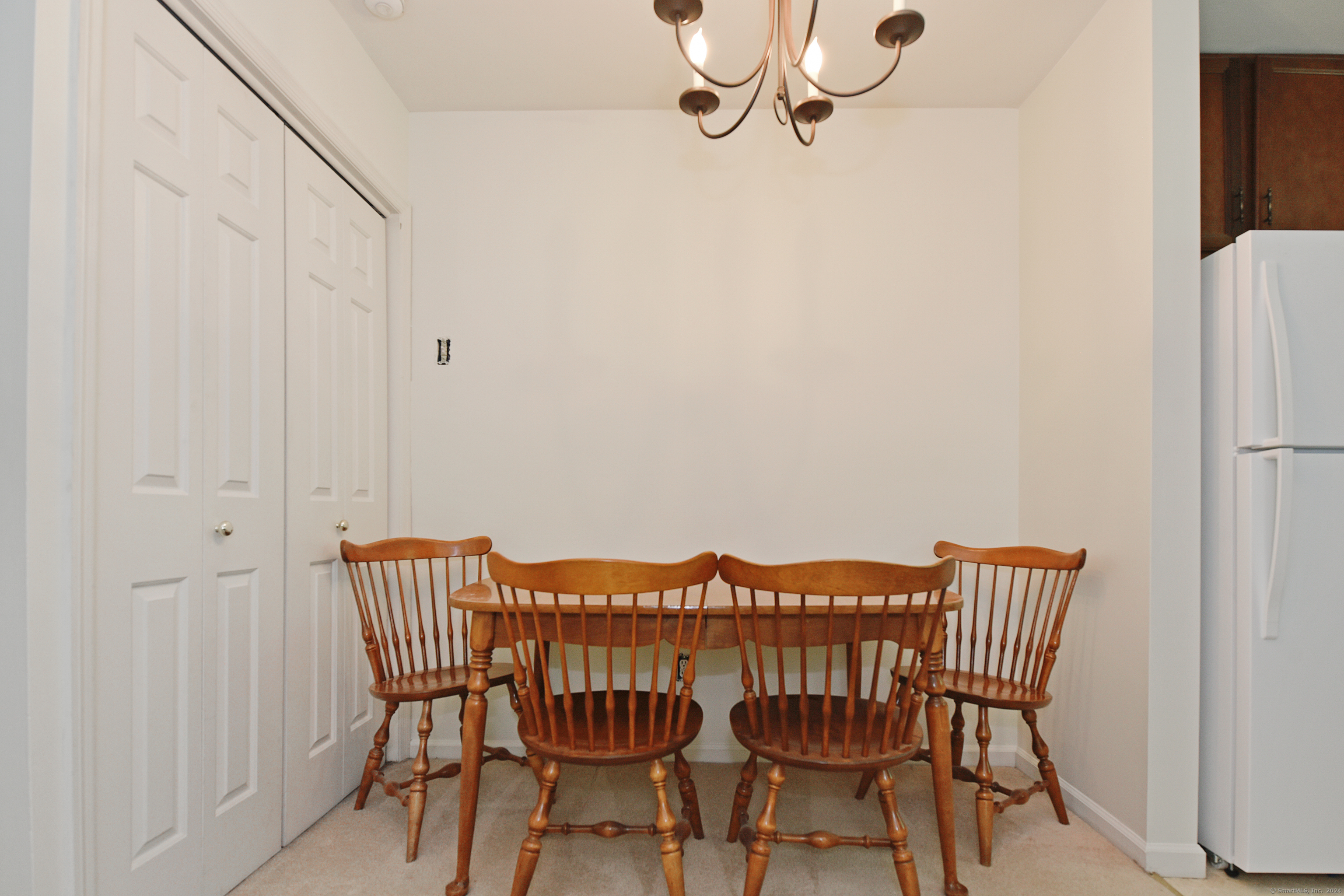 Dining area with a wooden table and four spindle-back chairs beside white closet doors and a refrigerator.