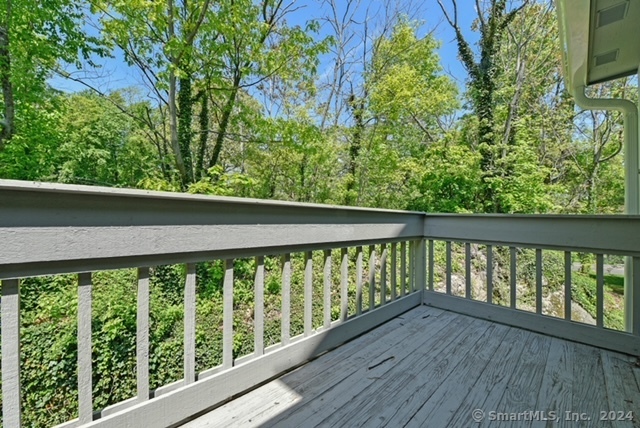 Gray wooden deck with railings overlooking leafy trees and greenery.