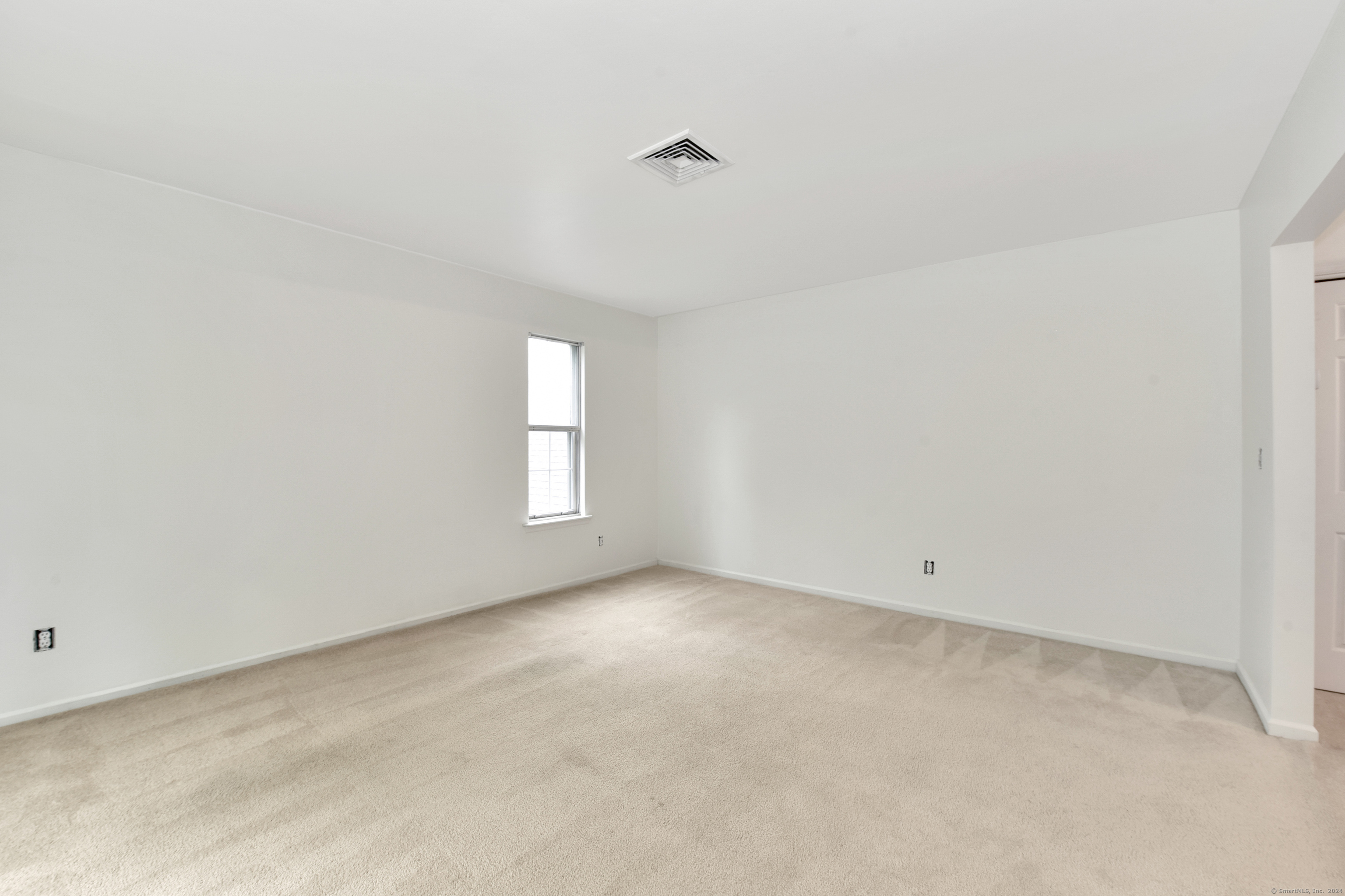 Empty carpeted room with white walls and a narrow window.