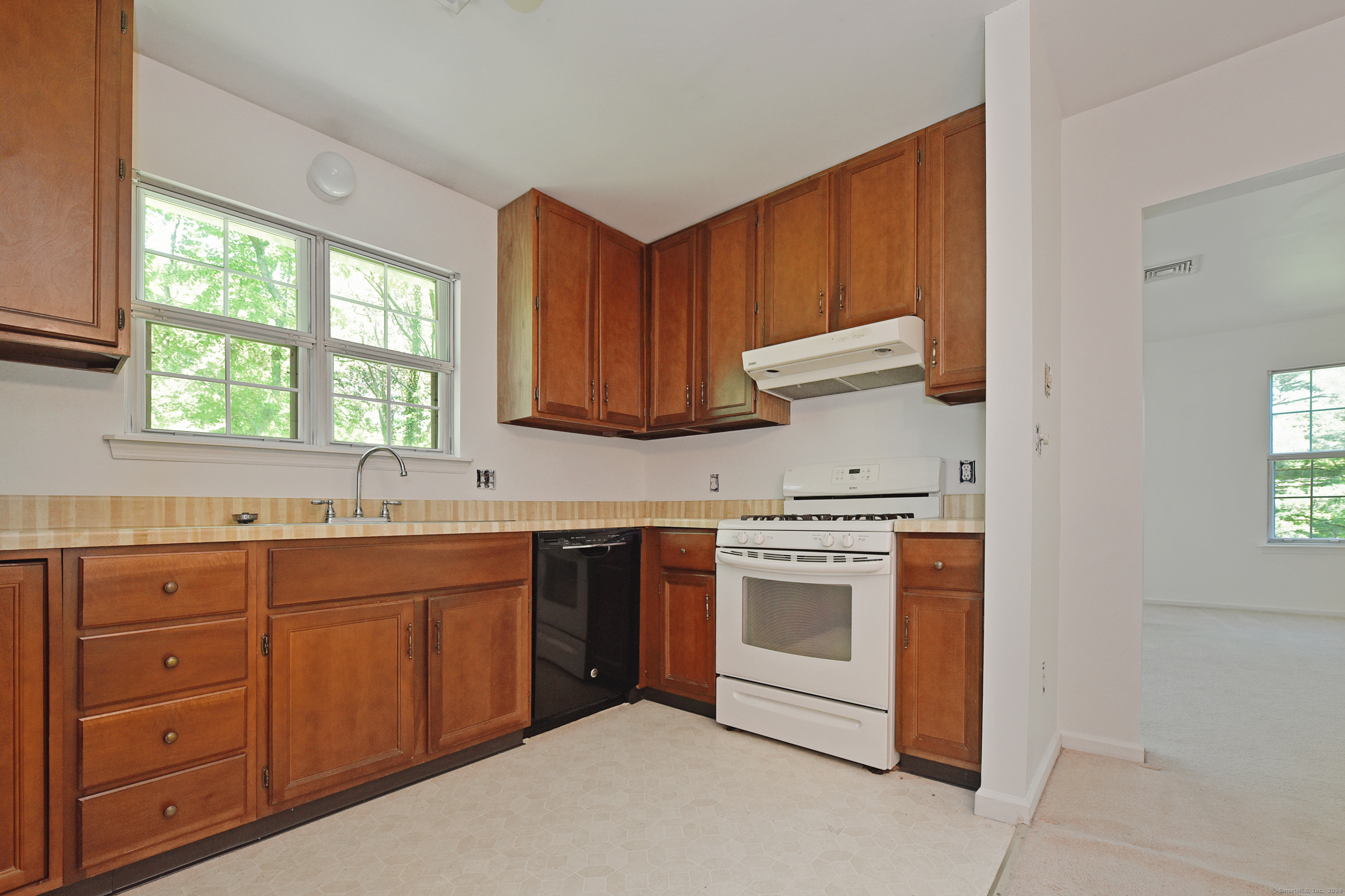 Kitchen with reddish-brown wood cabinets, a sink beneath two windows, white stove, and black dishwasher.