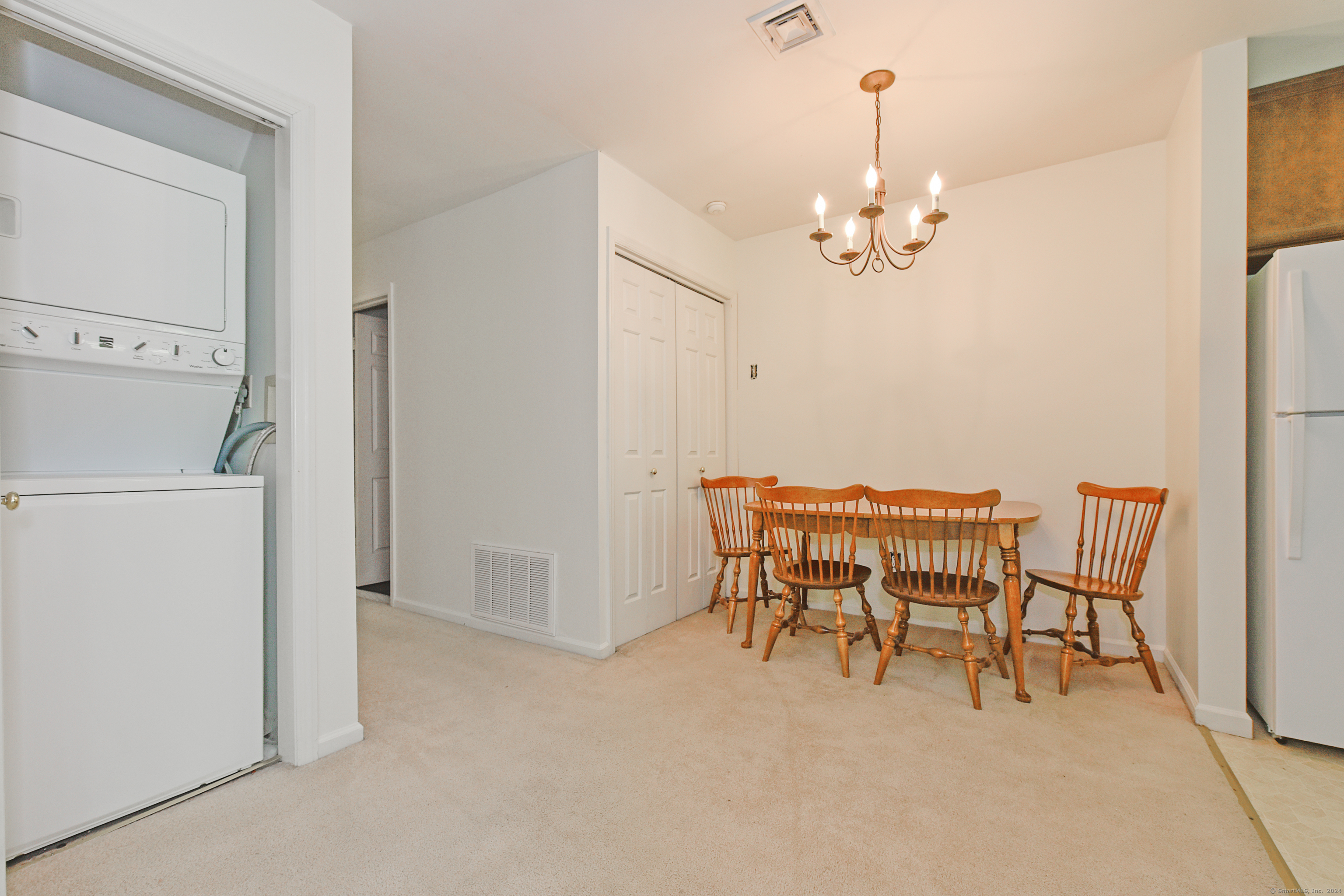 Dining area with a wooden table and chairs, chandelier, and stacked washer and dryer nearby.