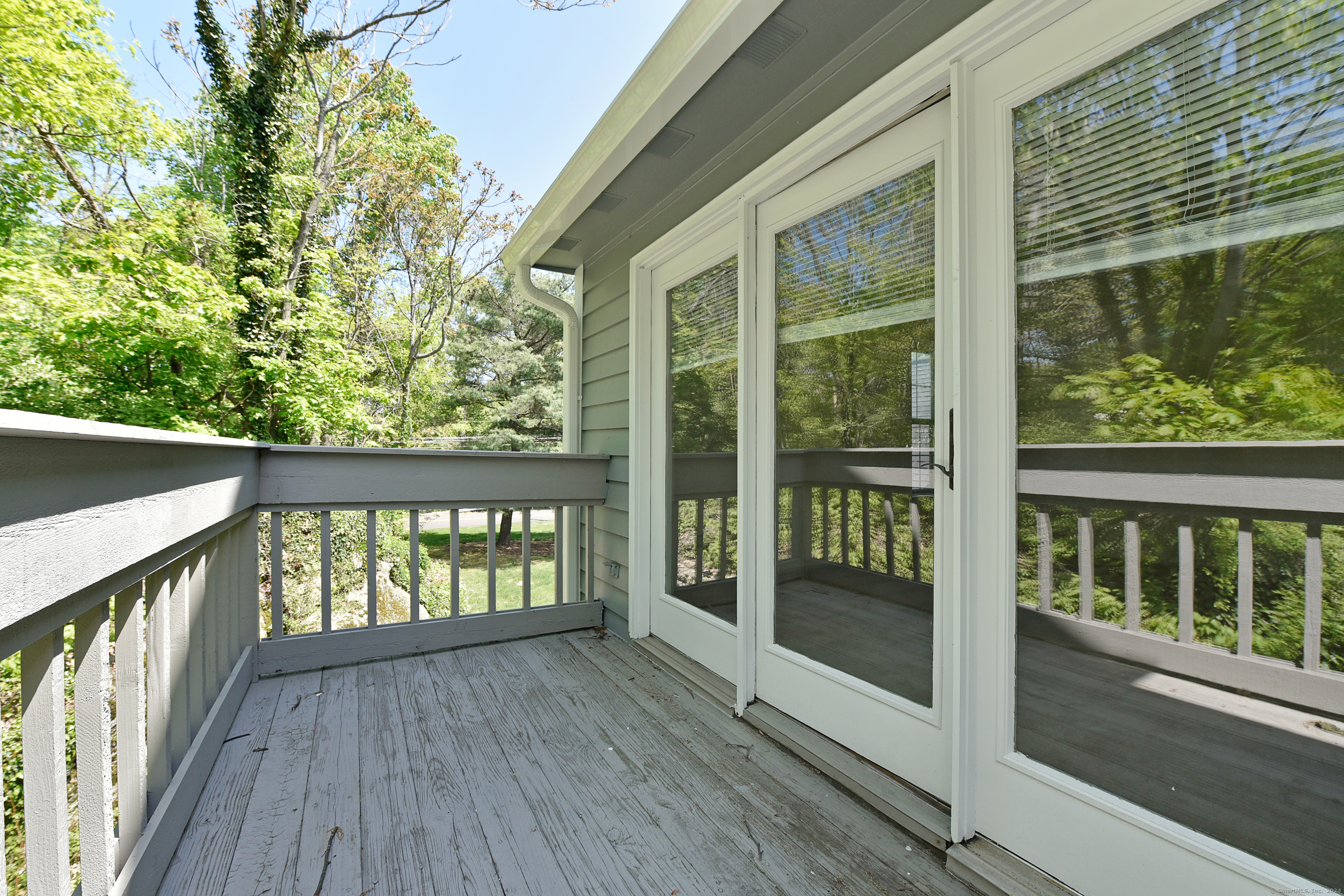 Gray balcony with weathered decking and white railings overlooking leafy trees.