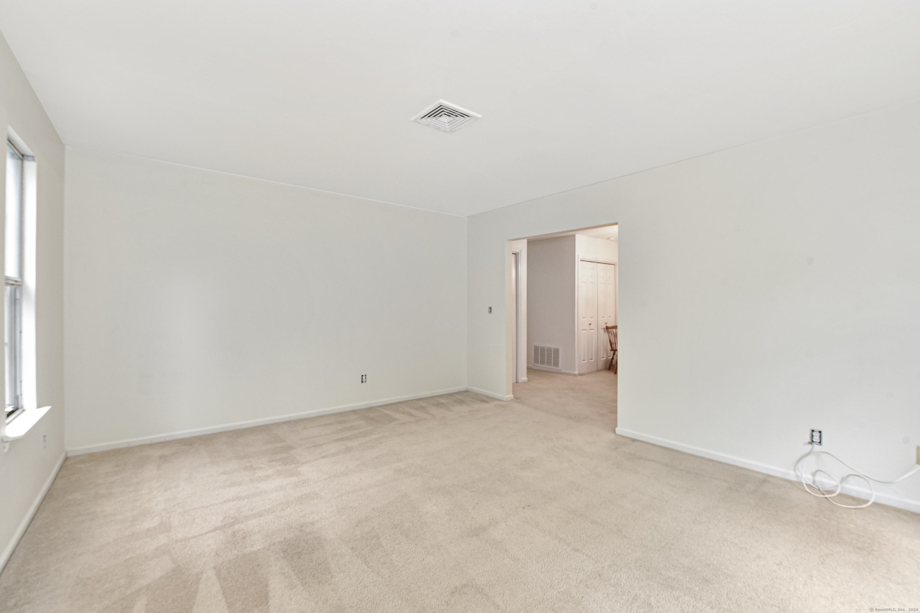 Empty carpeted living room with a window and an open doorway to an adjoining room.