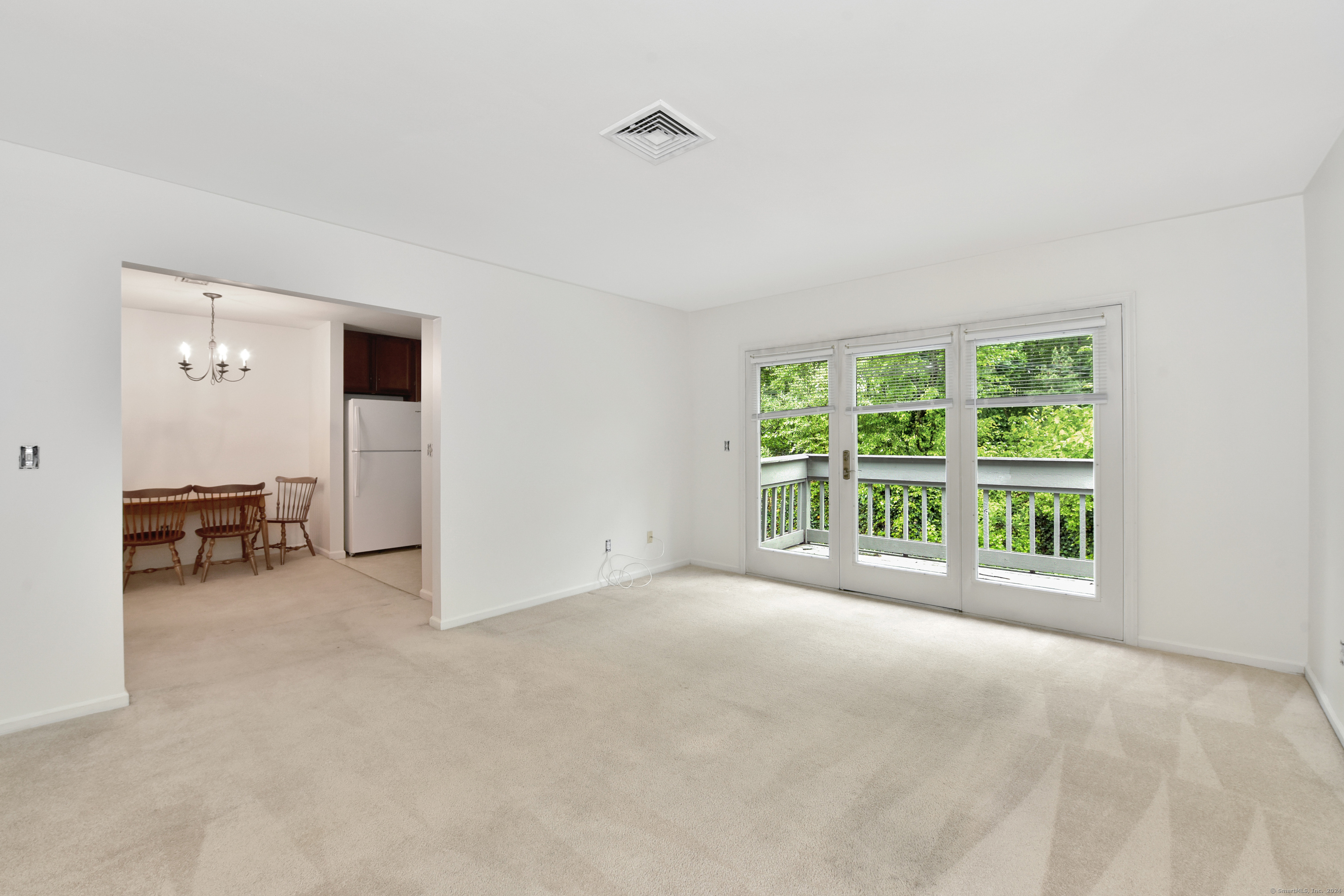 Living room with beige carpet and glass doors opening to a deck amid leafy trees.