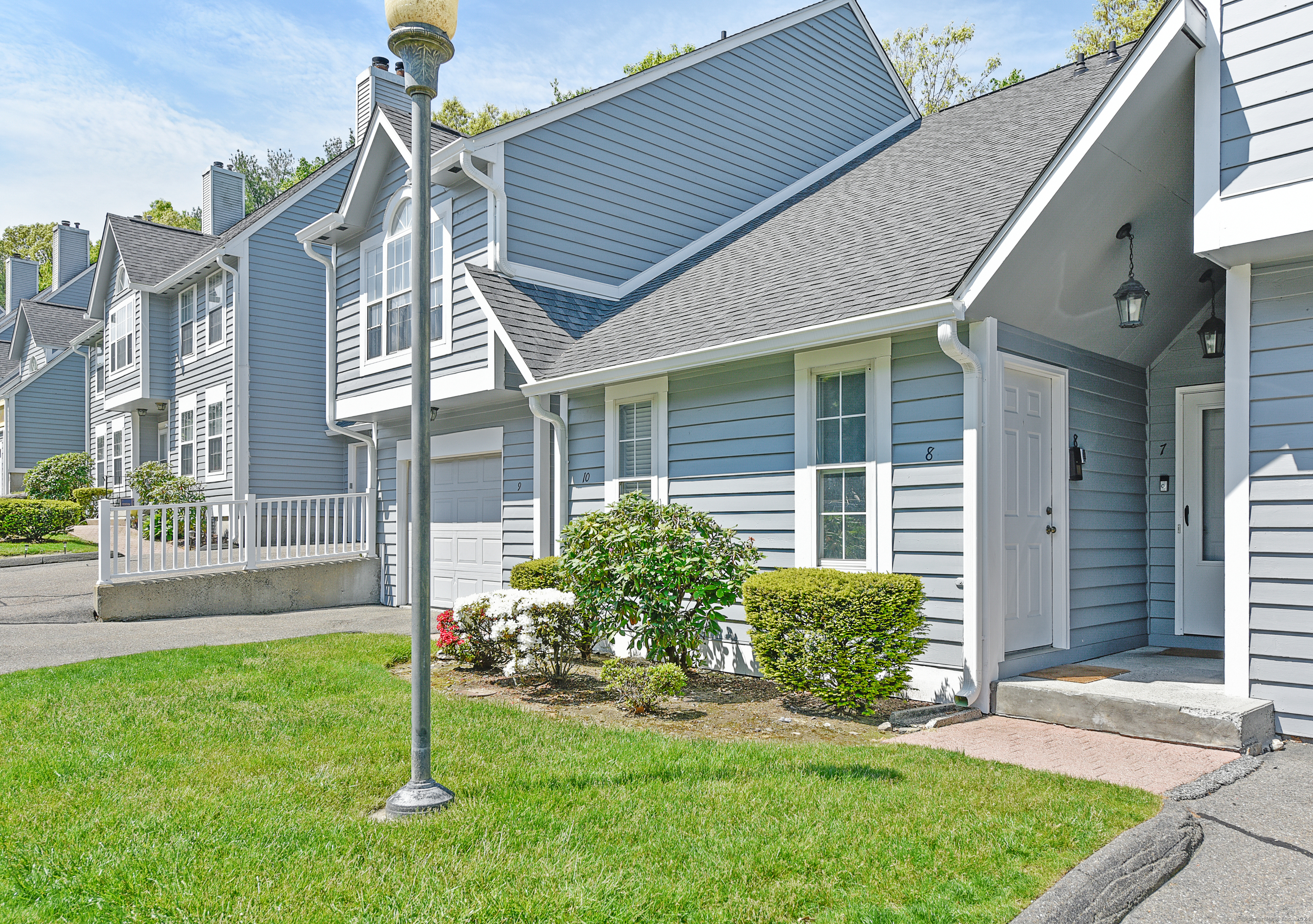 Blue-gray attached home marked 8, with white trim, a covered entry, front shrubs, and lawn.