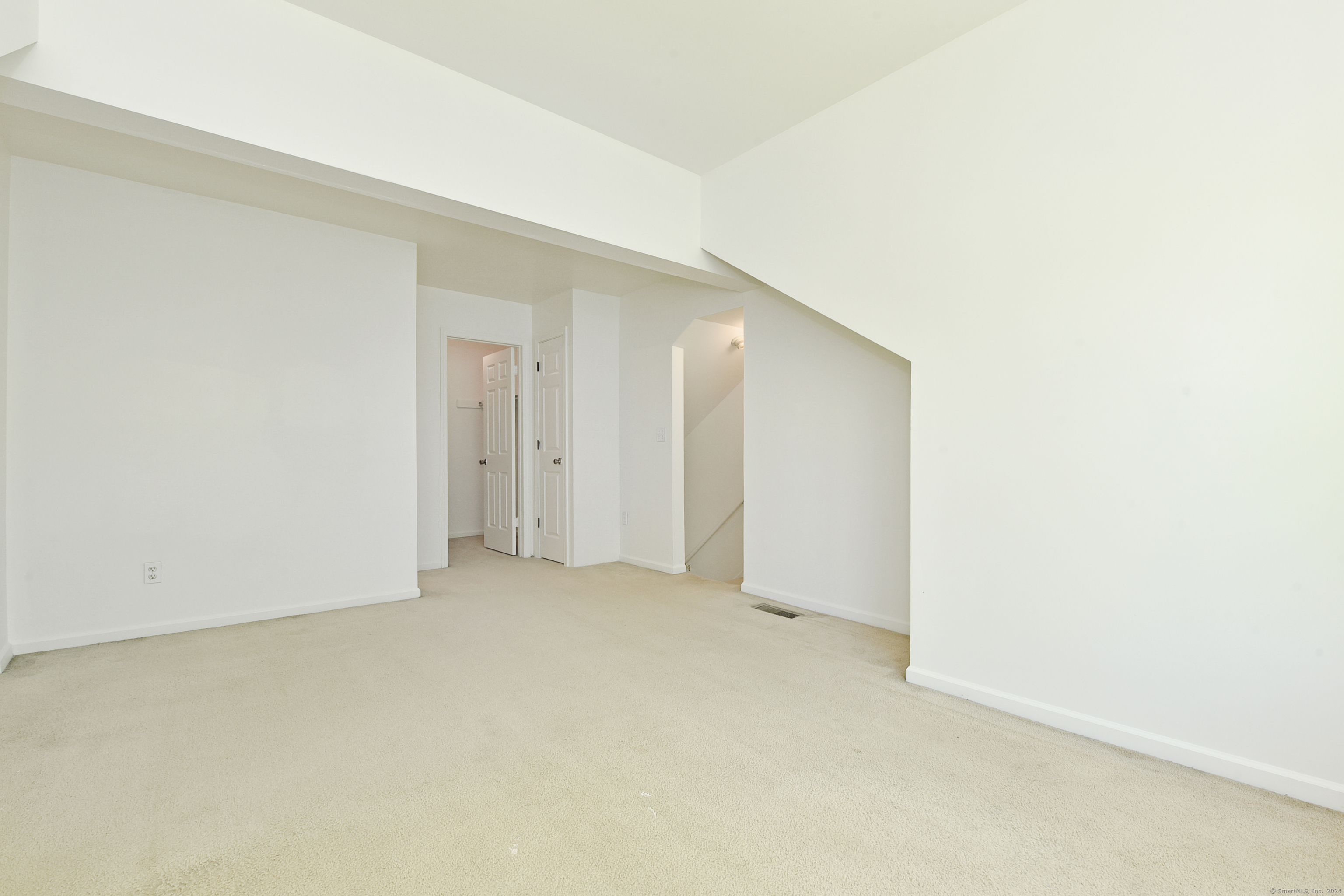 Empty carpeted room with an angled ceiling, doorway, and staircase.