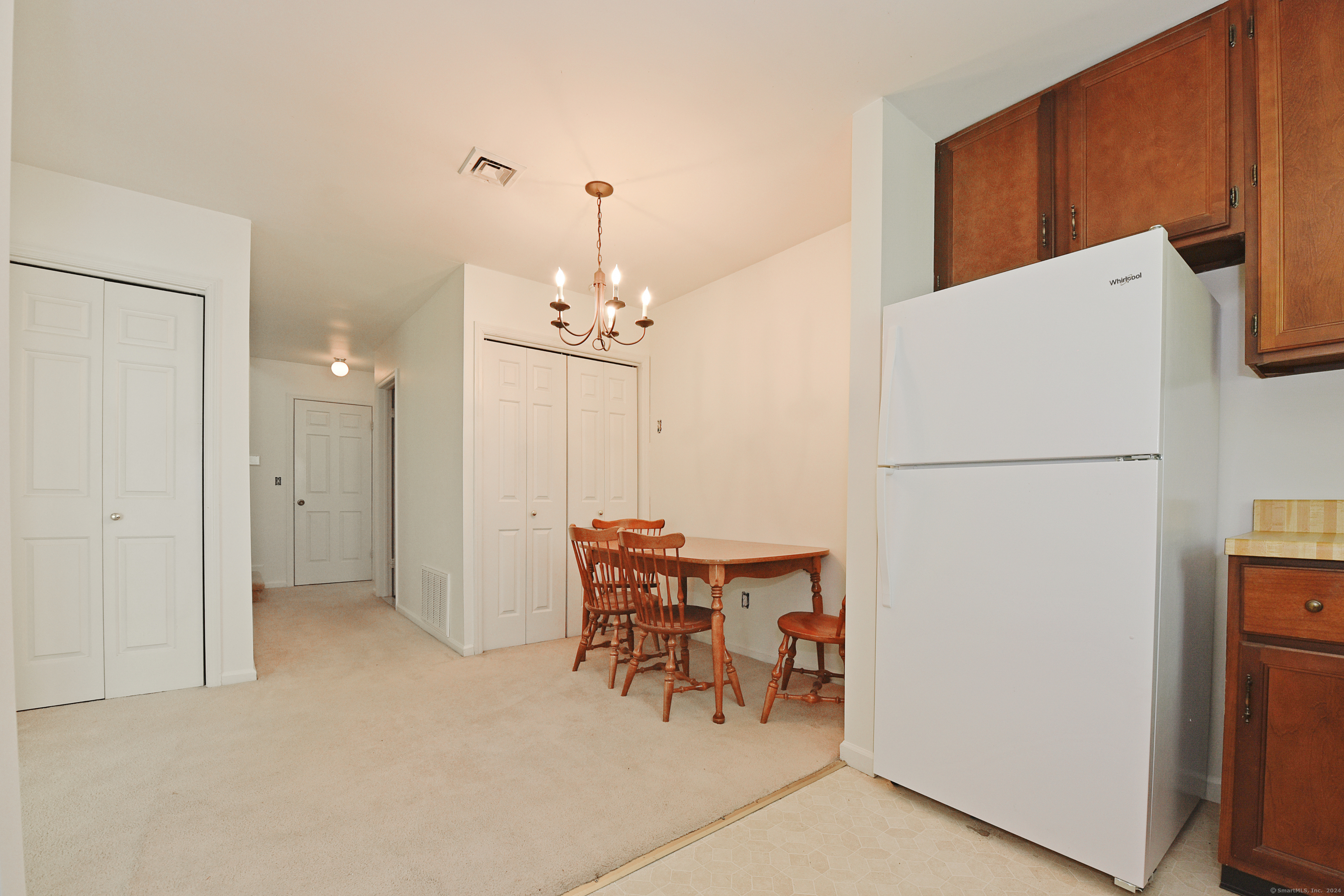 Kitchen and dining area with a white refrigerator and a wooden table beneath a chandelier.