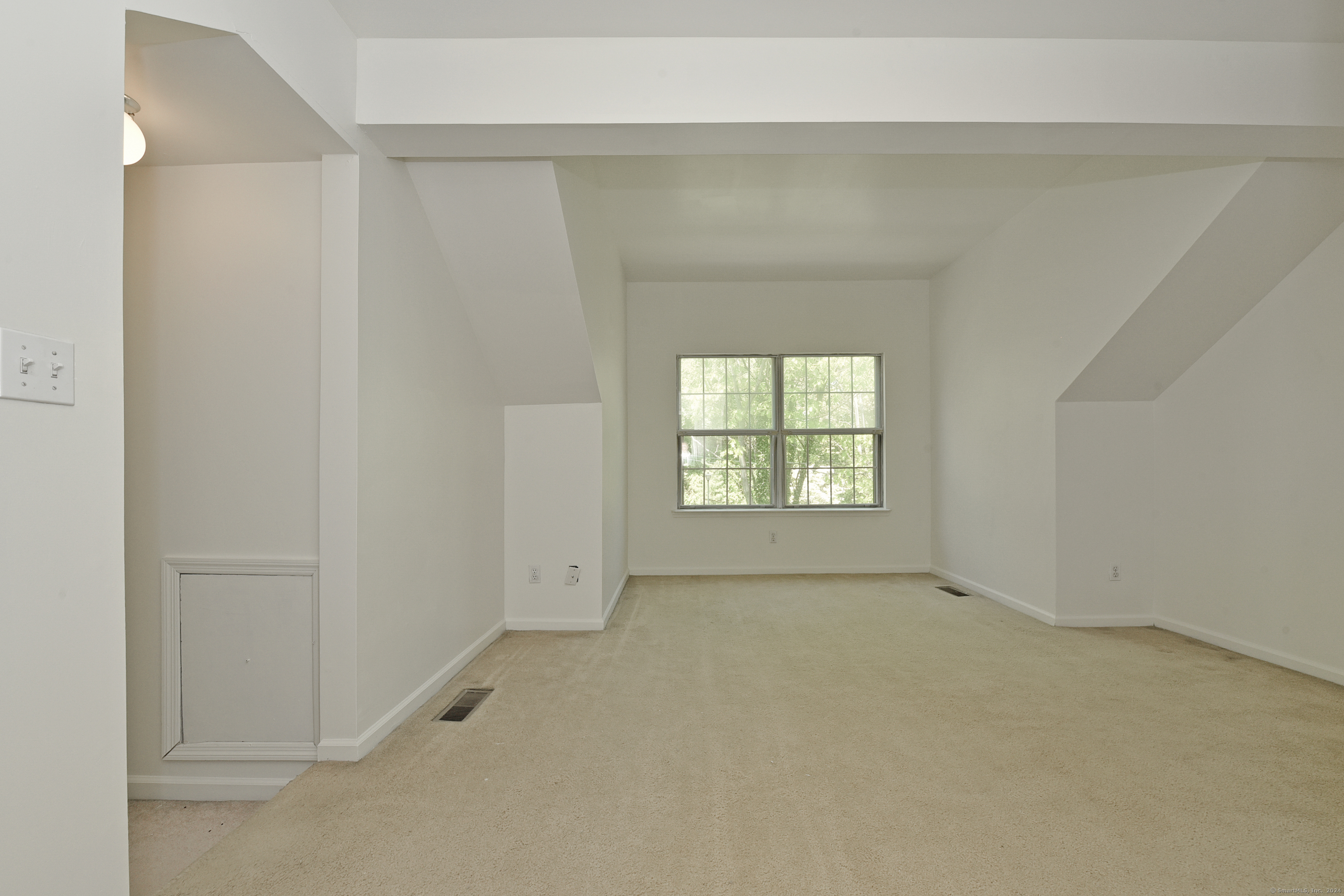 Vacant carpeted room with an angled ceiling and a divided-pane window overlooking trees.