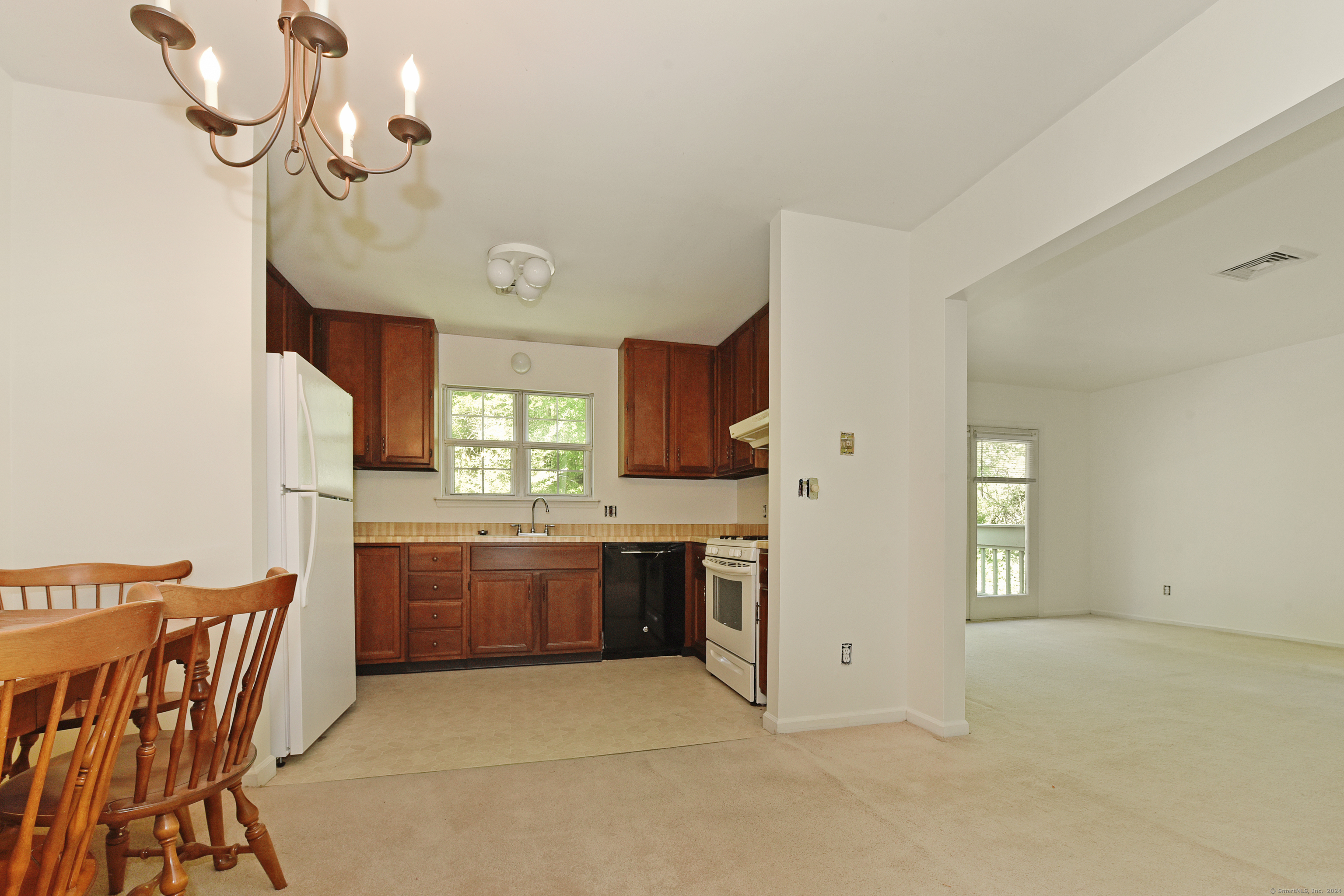 Kitchen with dark wood cabinets and white appliances, adjoining a carpeted living area.