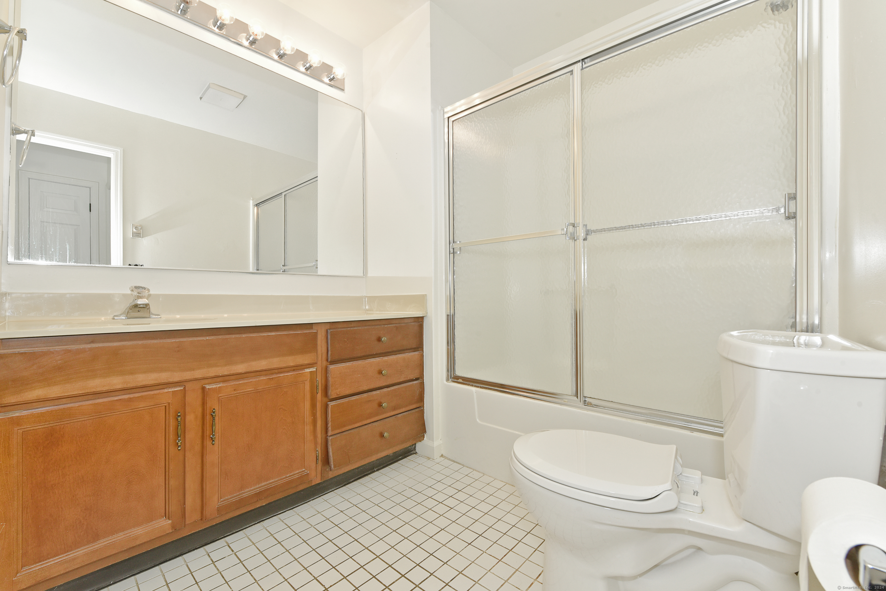 Bathroom with a long wood vanity, frosted-glass tub and shower, and white tile floor.