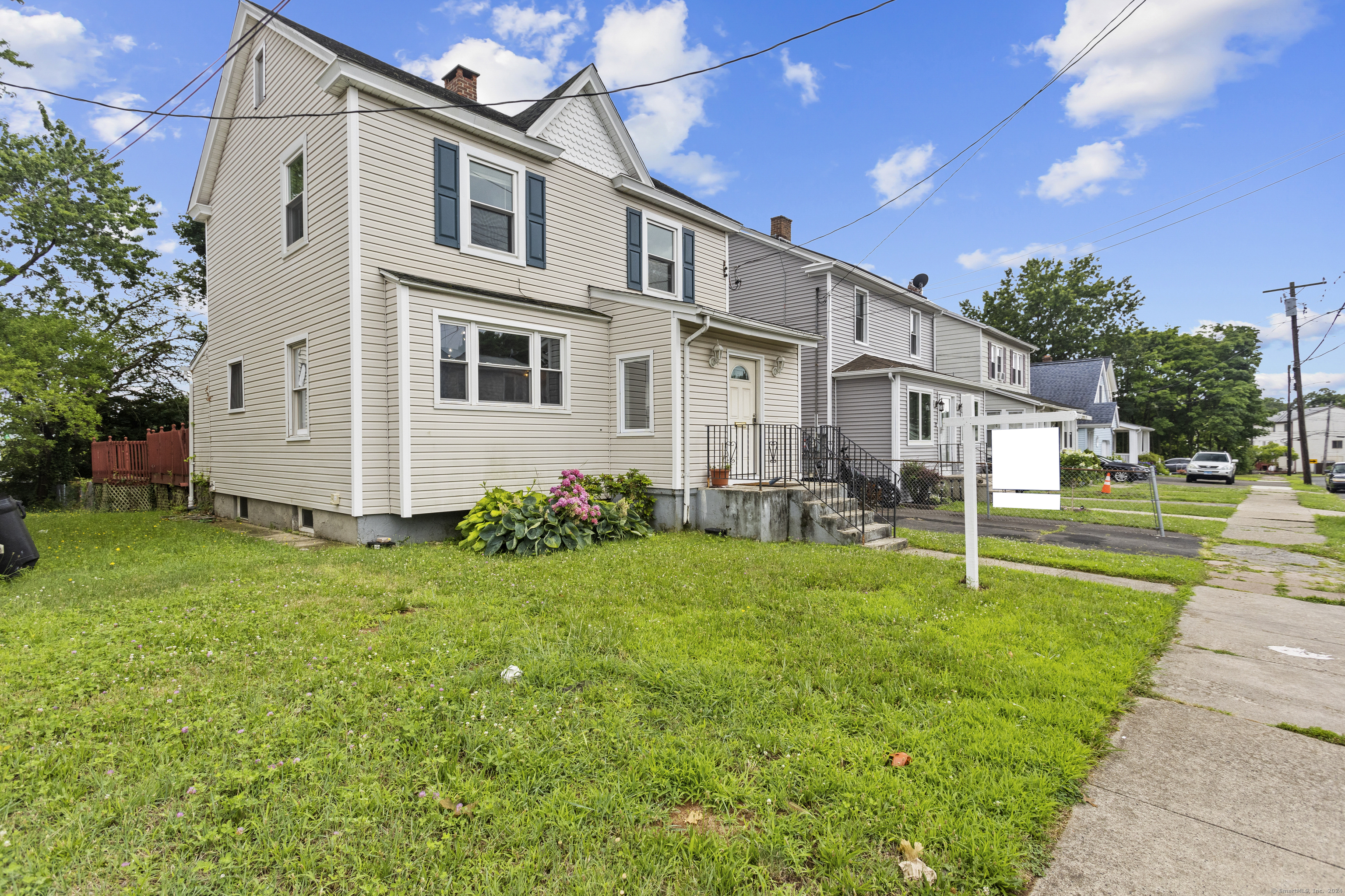 Beige two-story house with dark shutters, front lawn, hydrangeas, and steps to the entrance.
