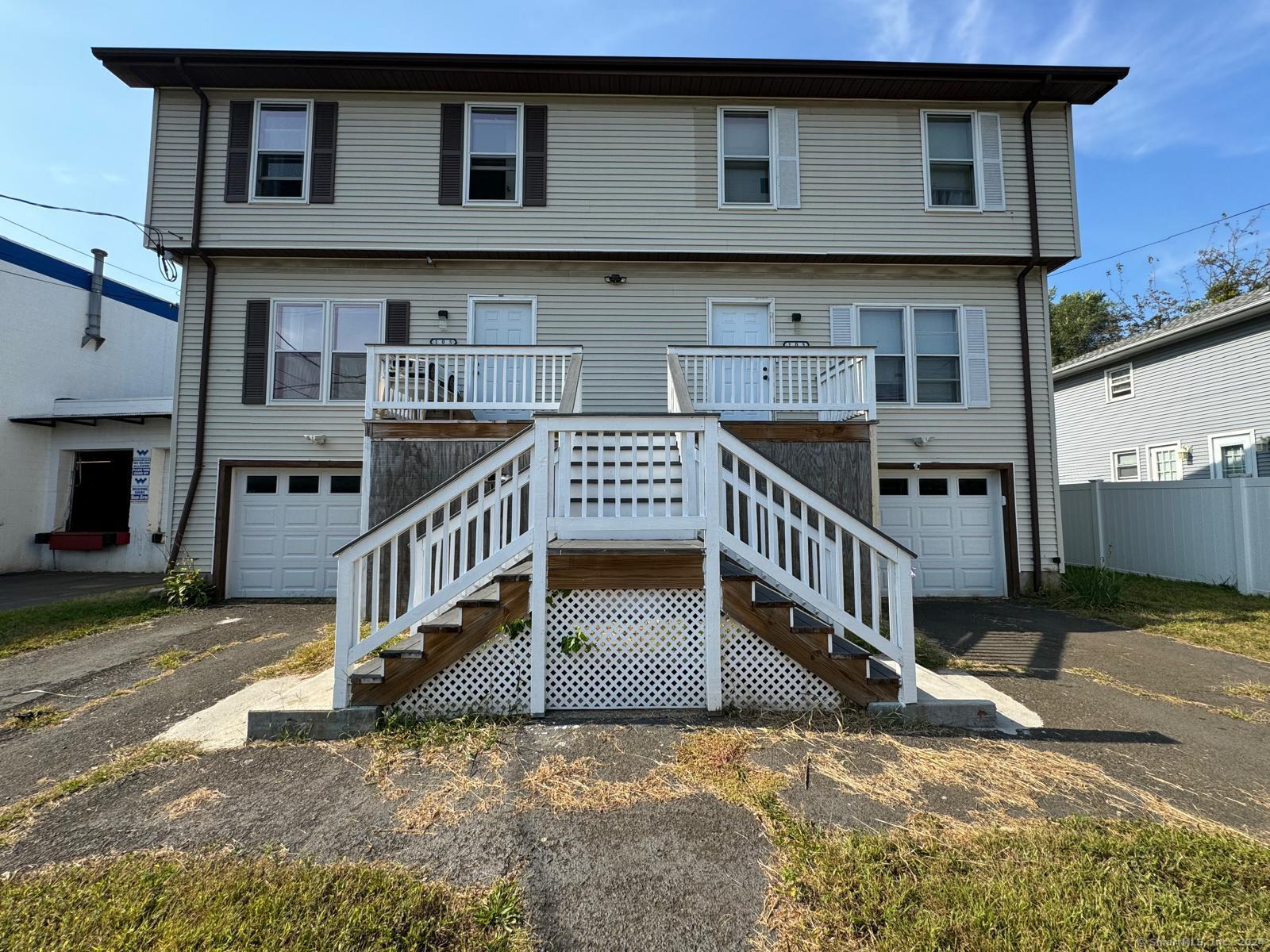 Two-story residence with multiple entrances, garages, and a central staircase with white railings.