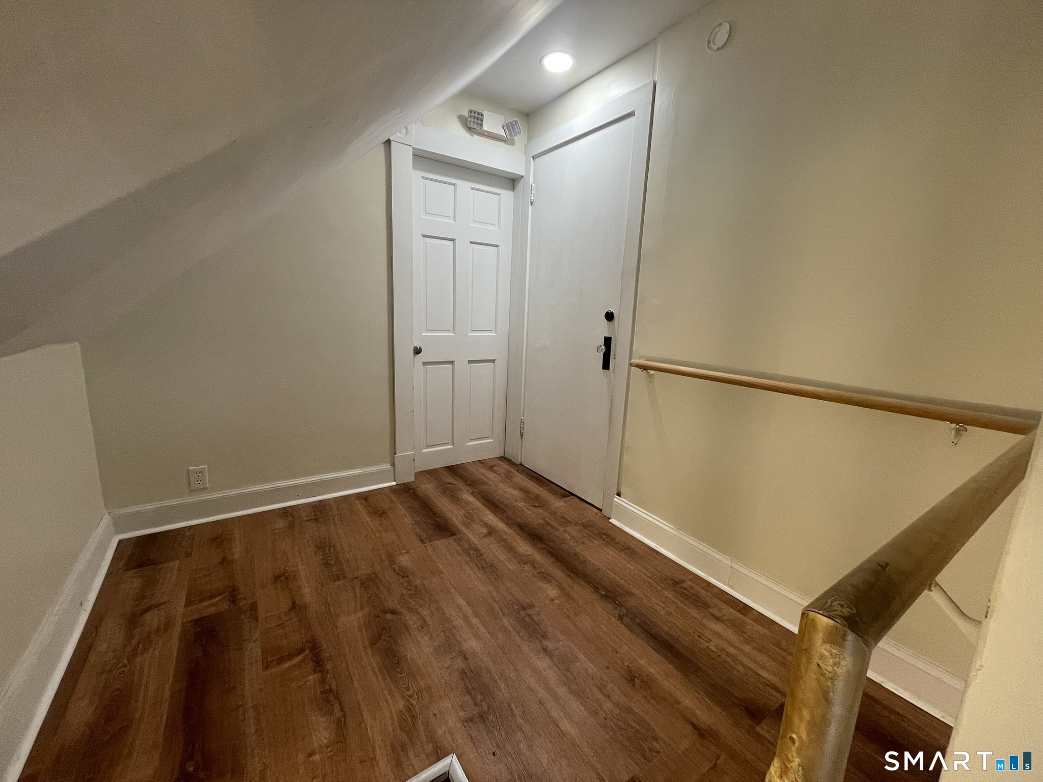 Landing with dark wood flooring, two white doors, and a wooden stair railing.
