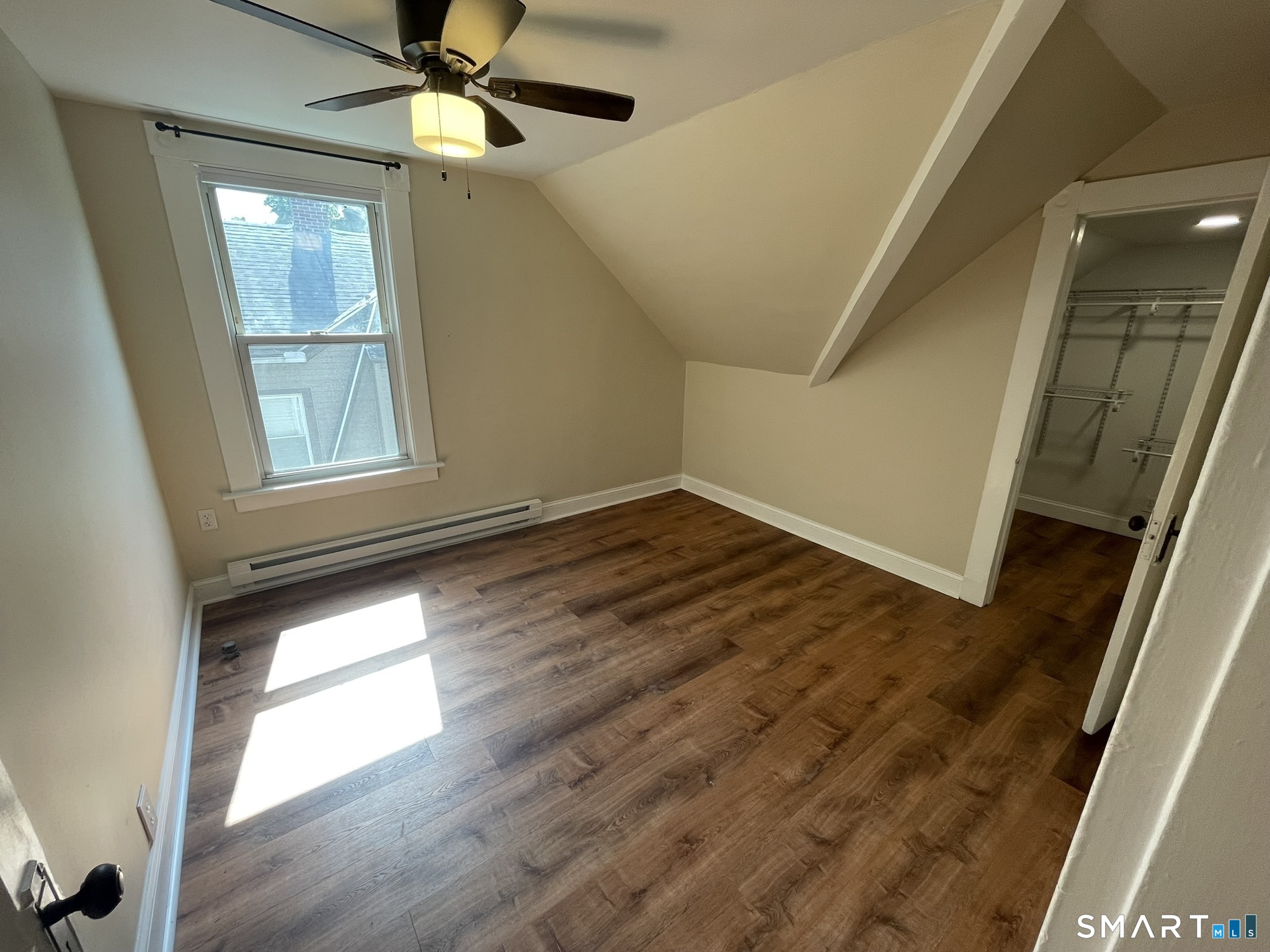 Empty attic bedroom with sloped ceilings, wood-look floors, a window, and an open closet.