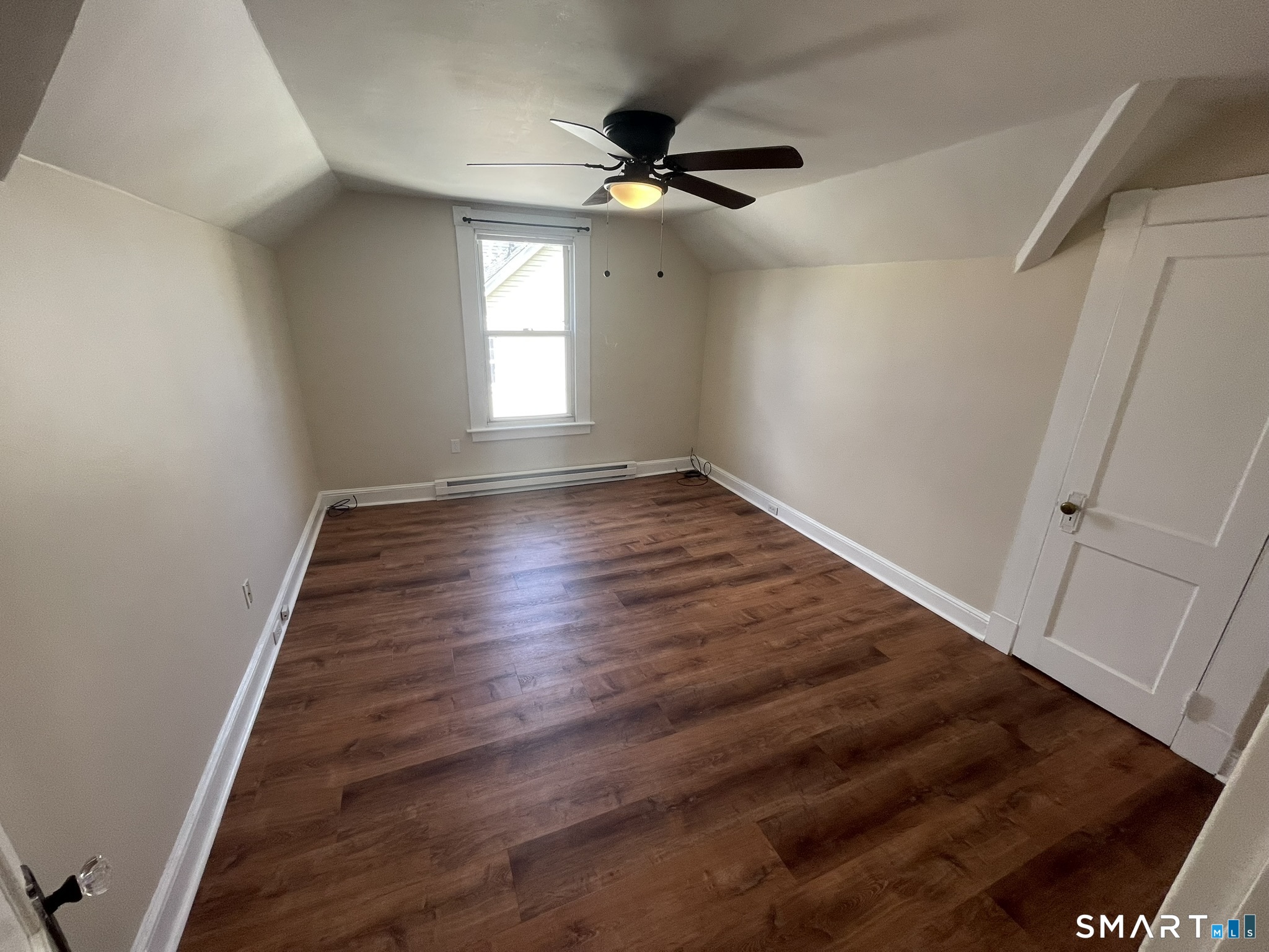 Empty room with sloped ceilings, dark wood-look flooring, and a ceiling fan.
