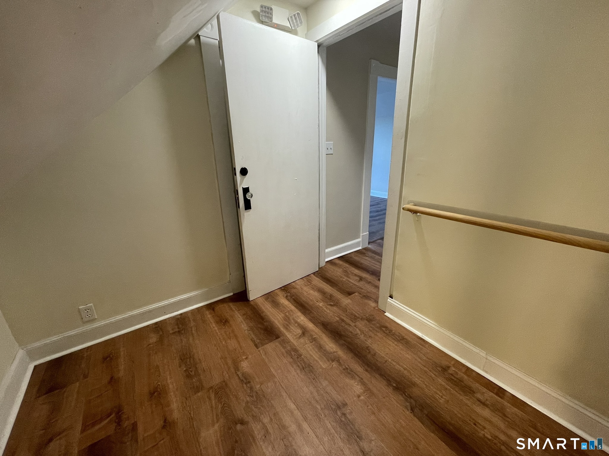 Entry hall with an open white door, brown wood flooring, and a wooden handrail.