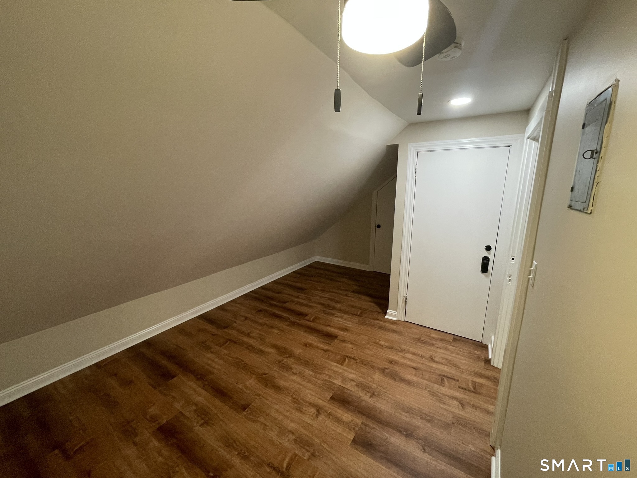 Empty entryway with wood-look flooring, a sloped ceiling, and a white door.