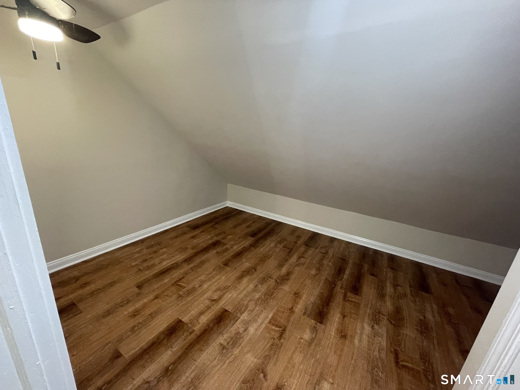 Empty upper-level room with a sloped ceiling, wood flooring, and a ceiling fan.