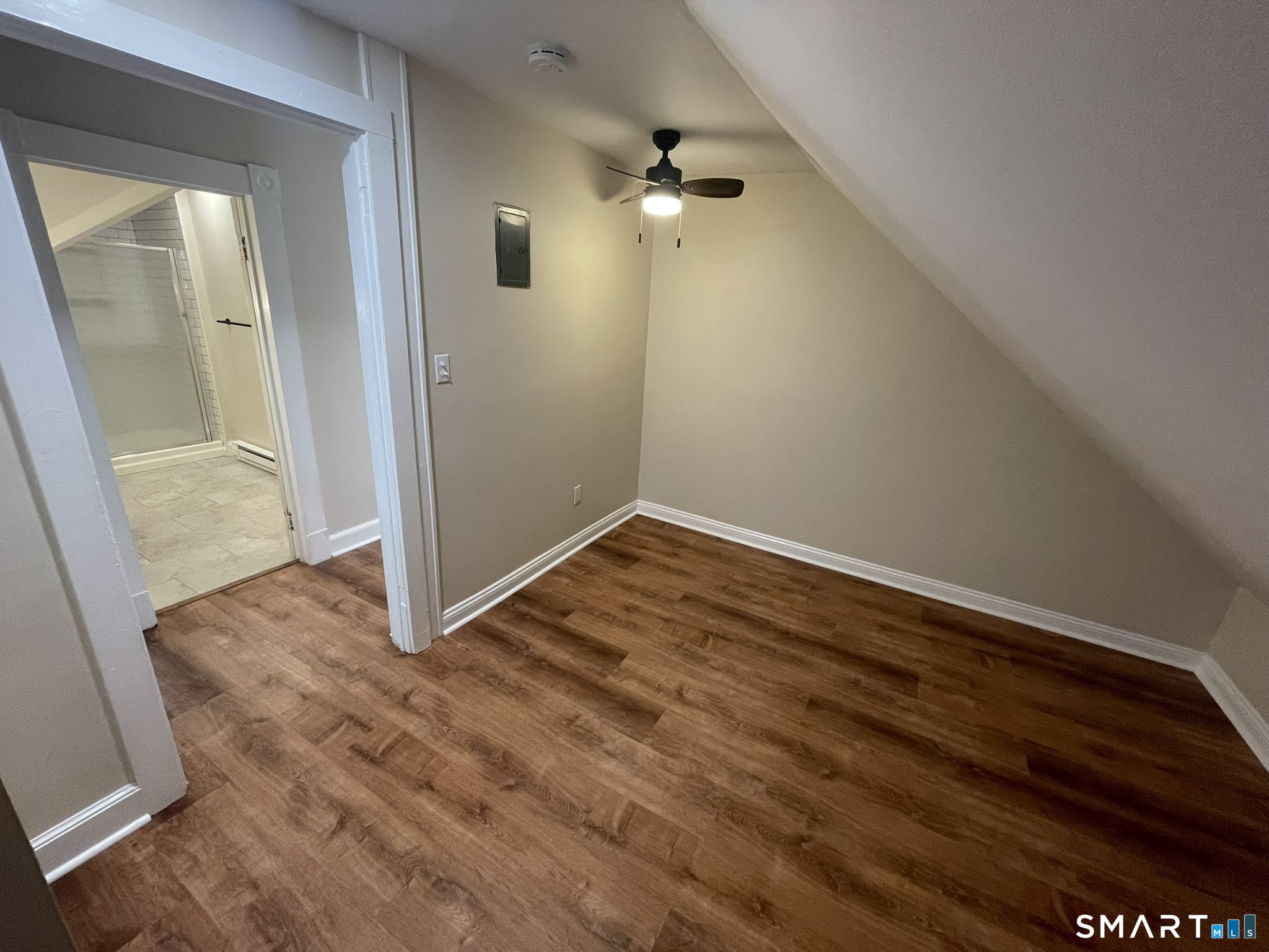 Empty room with wood-look flooring, a sloped ceiling, and an adjoining bathroom.