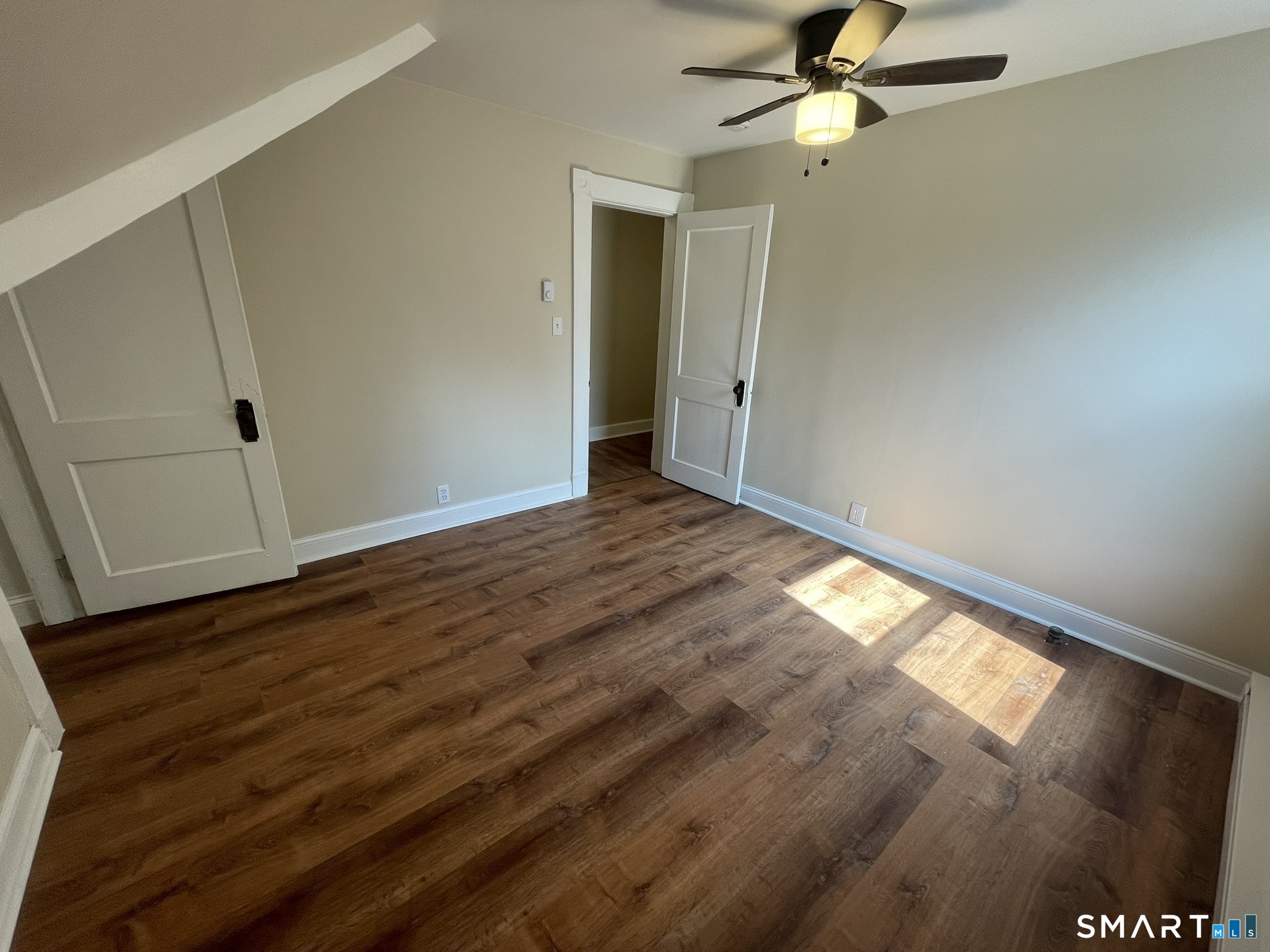Empty room with brown wood-look flooring, beige walls, and a ceiling fan.