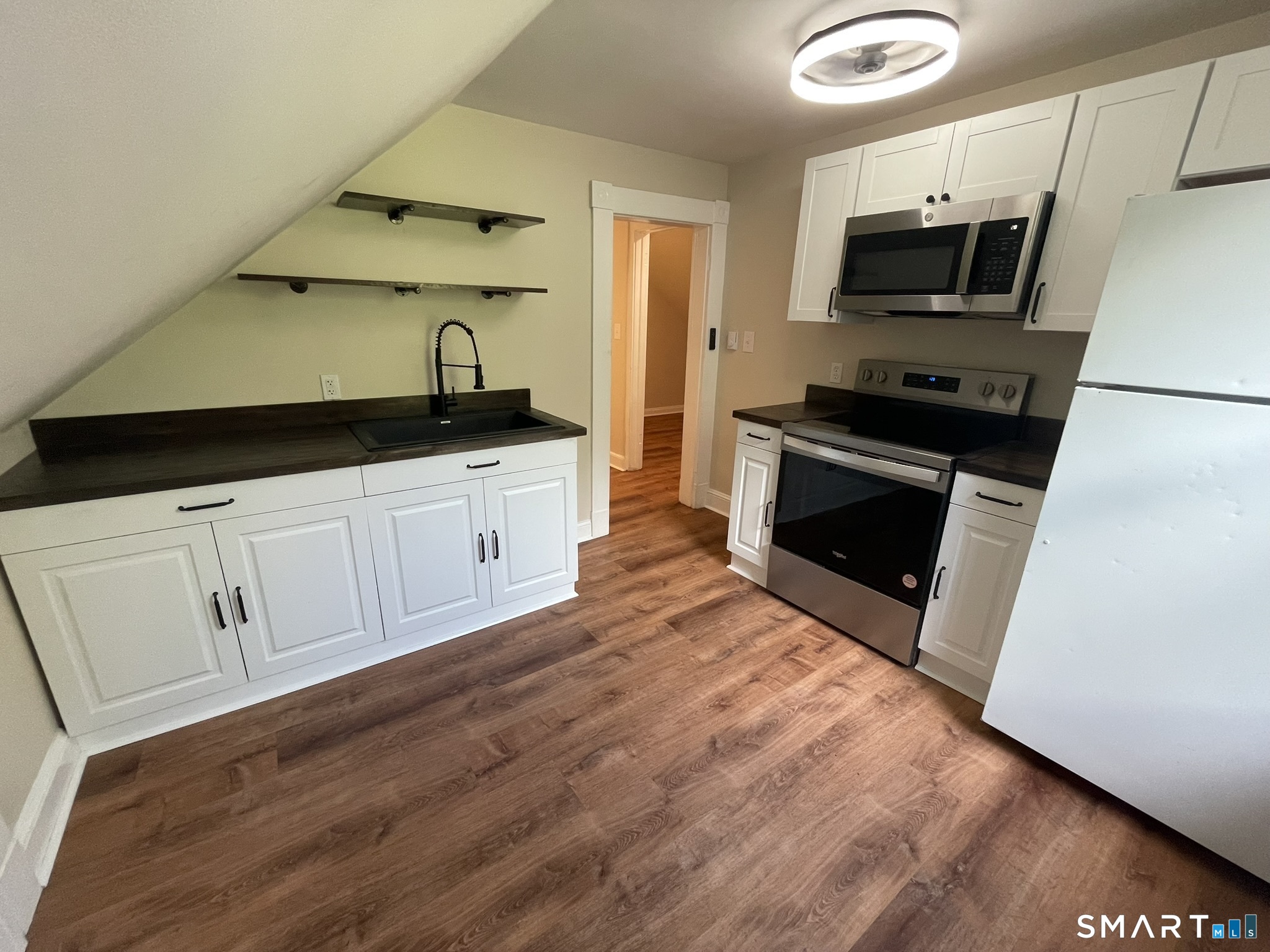 Kitchen with white cabinets, dark countertops, stainless steel appliances, and wood-look flooring beneath a sloped ceiling.