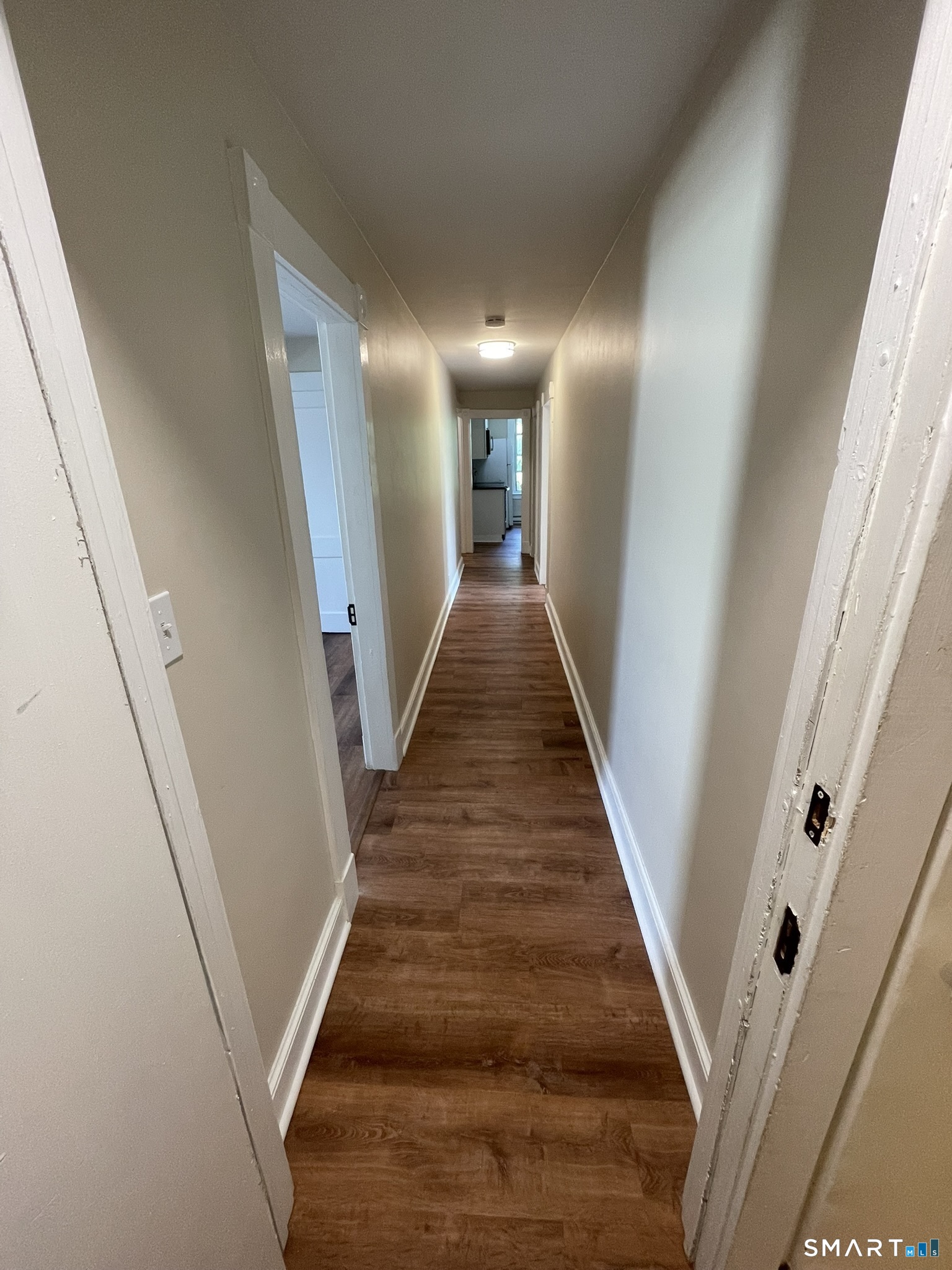 Interior hallway with wood-look flooring and beige walls, leading toward a kitchen.