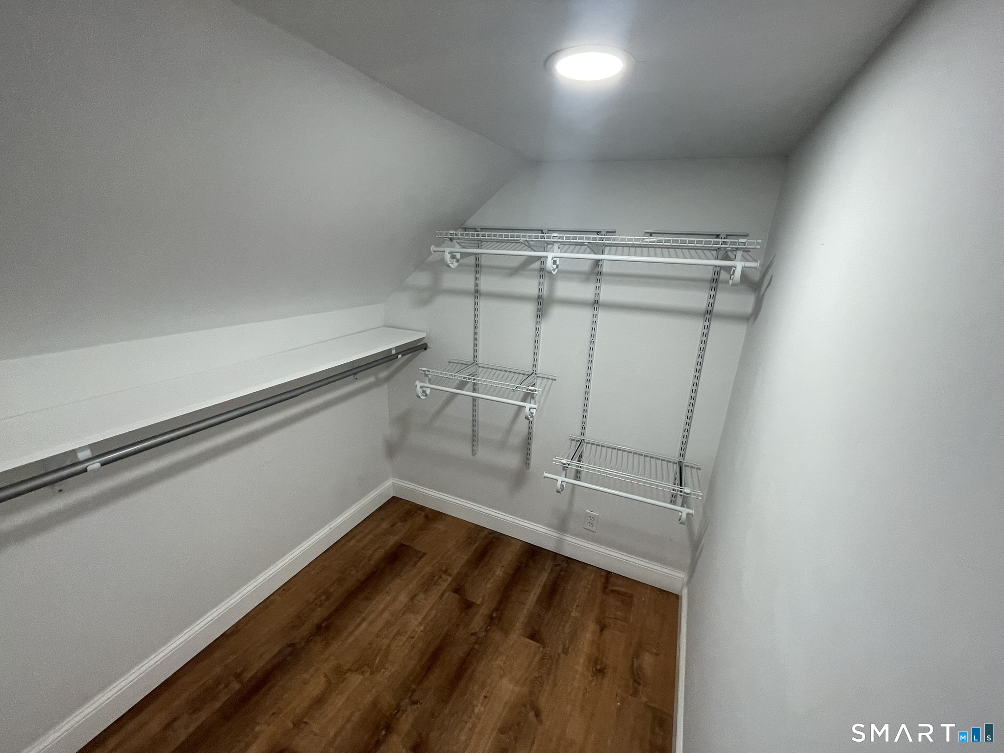 Walk-in closet with built-in wire shelving, hanging rods, and dark wood flooring.