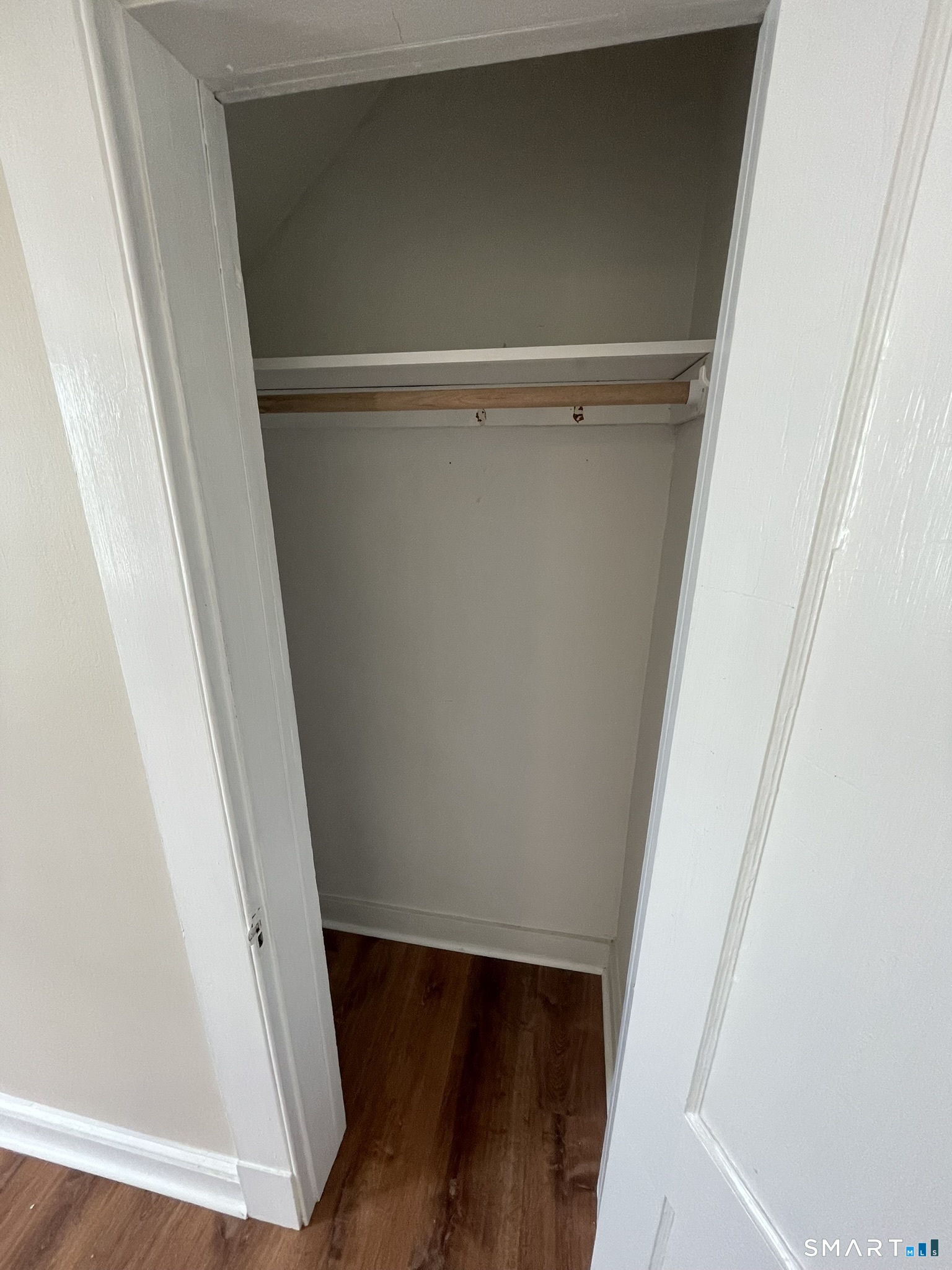 Empty built-in closet with an upper shelf, wooden hanging rod, and dark wood flooring.