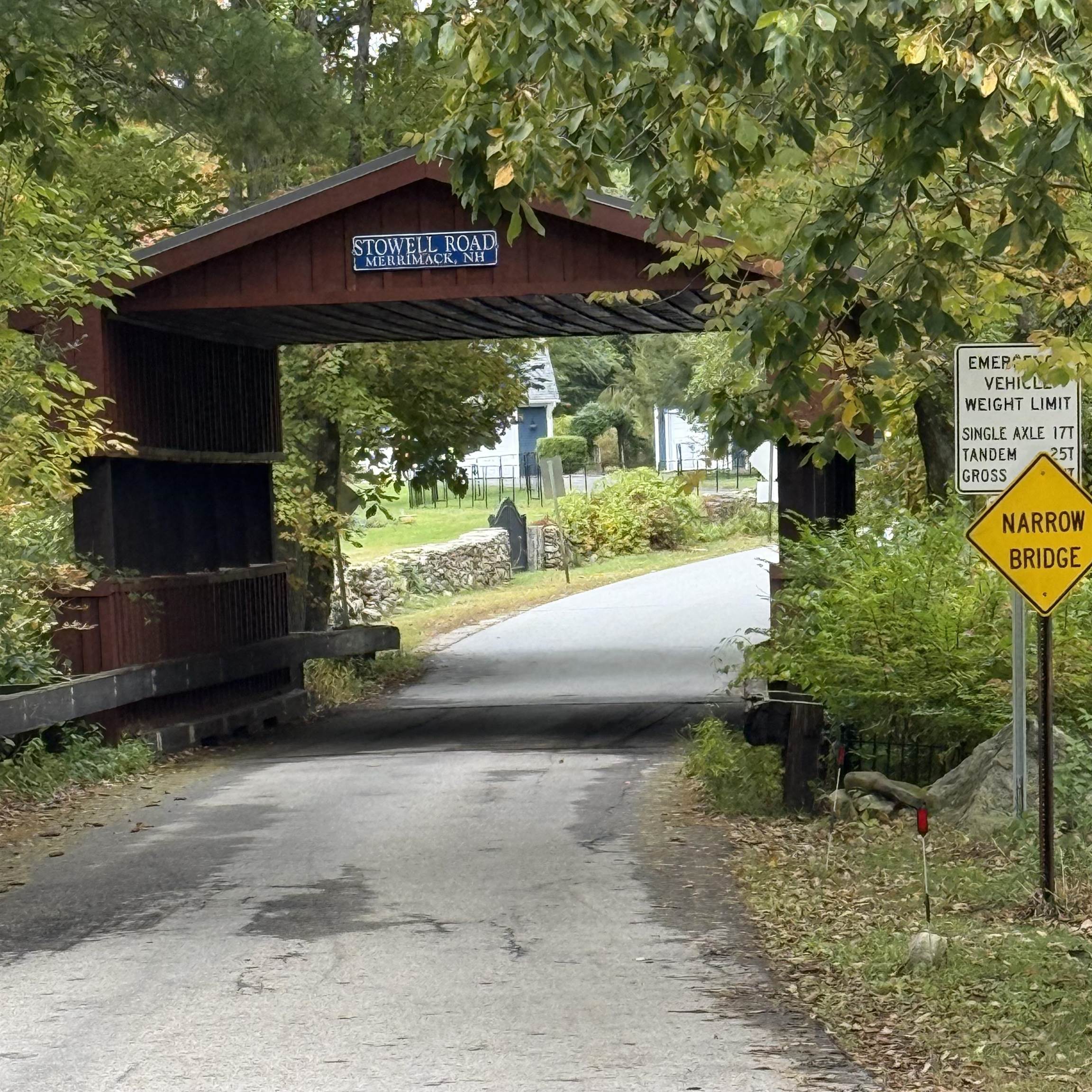 Covered wooden bridge on Stowell Road in Merrimack, New Hampshire, beneath leafy trees.