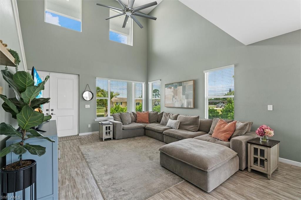 Vaulted living room with a gray sectional, high windows, and ceiling fan.