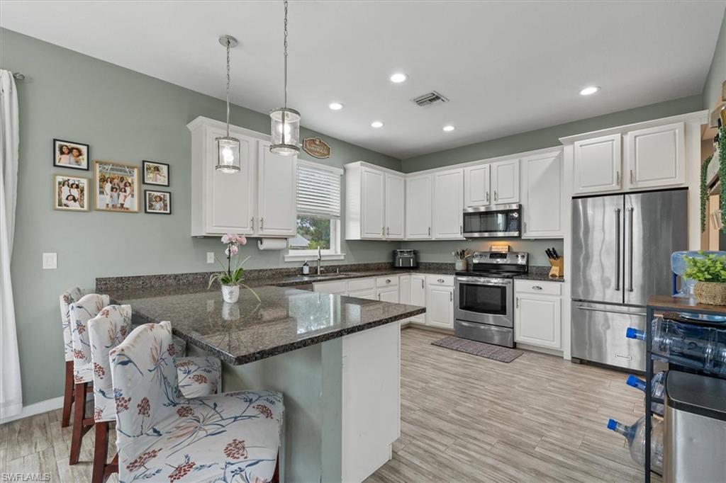 Kitchen with white cabinets, granite island, stainless steel appliances, and upholstered seating.