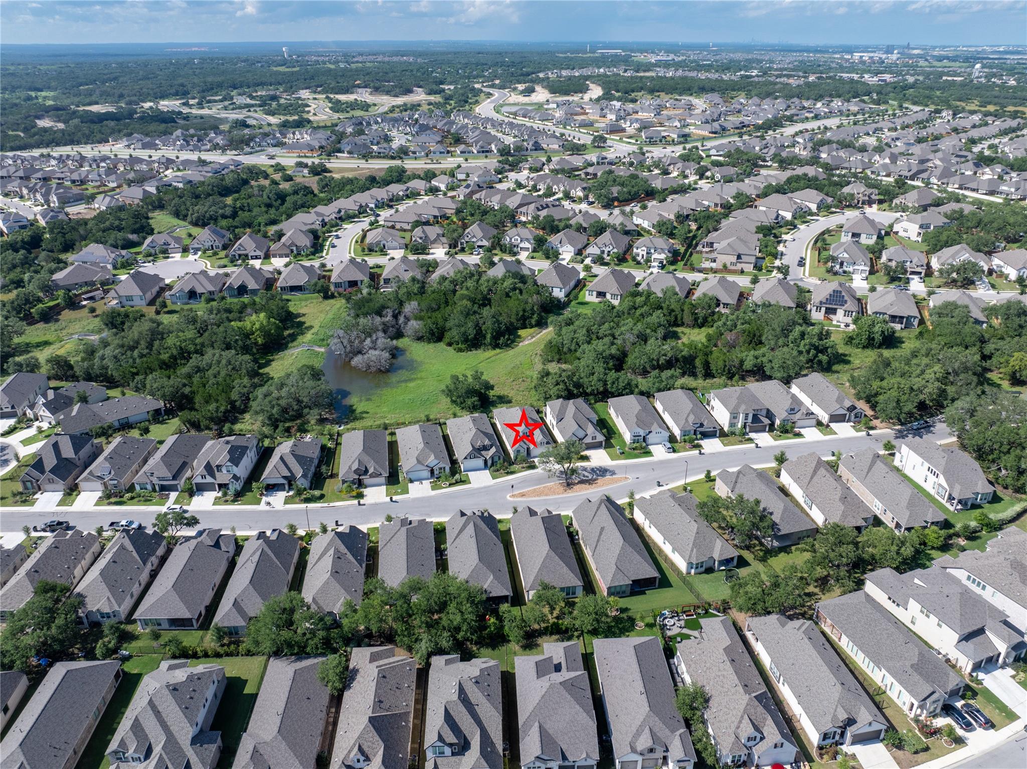 Aerial view of the marked home beside a tree-lined greenbelt and pond in a residential neighborhood.