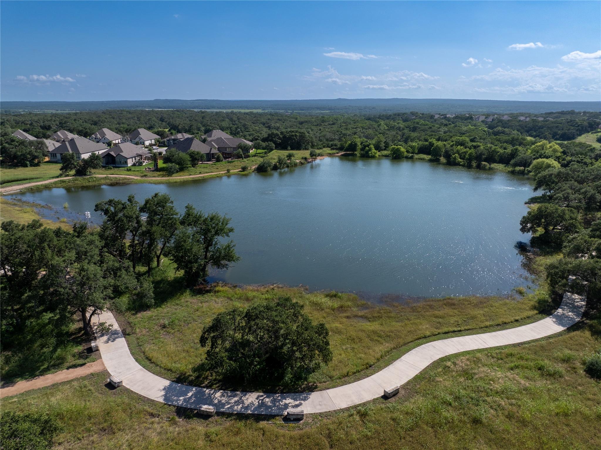 Aerial view of a neighborhood lake bordered by homes, trees, and a curved walking path.
