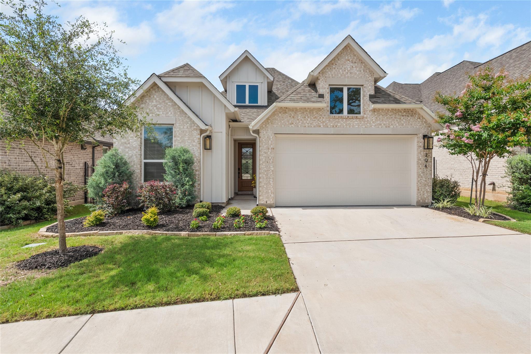 Front of a brick-and-siding home with a two-car garage and landscaped yard.