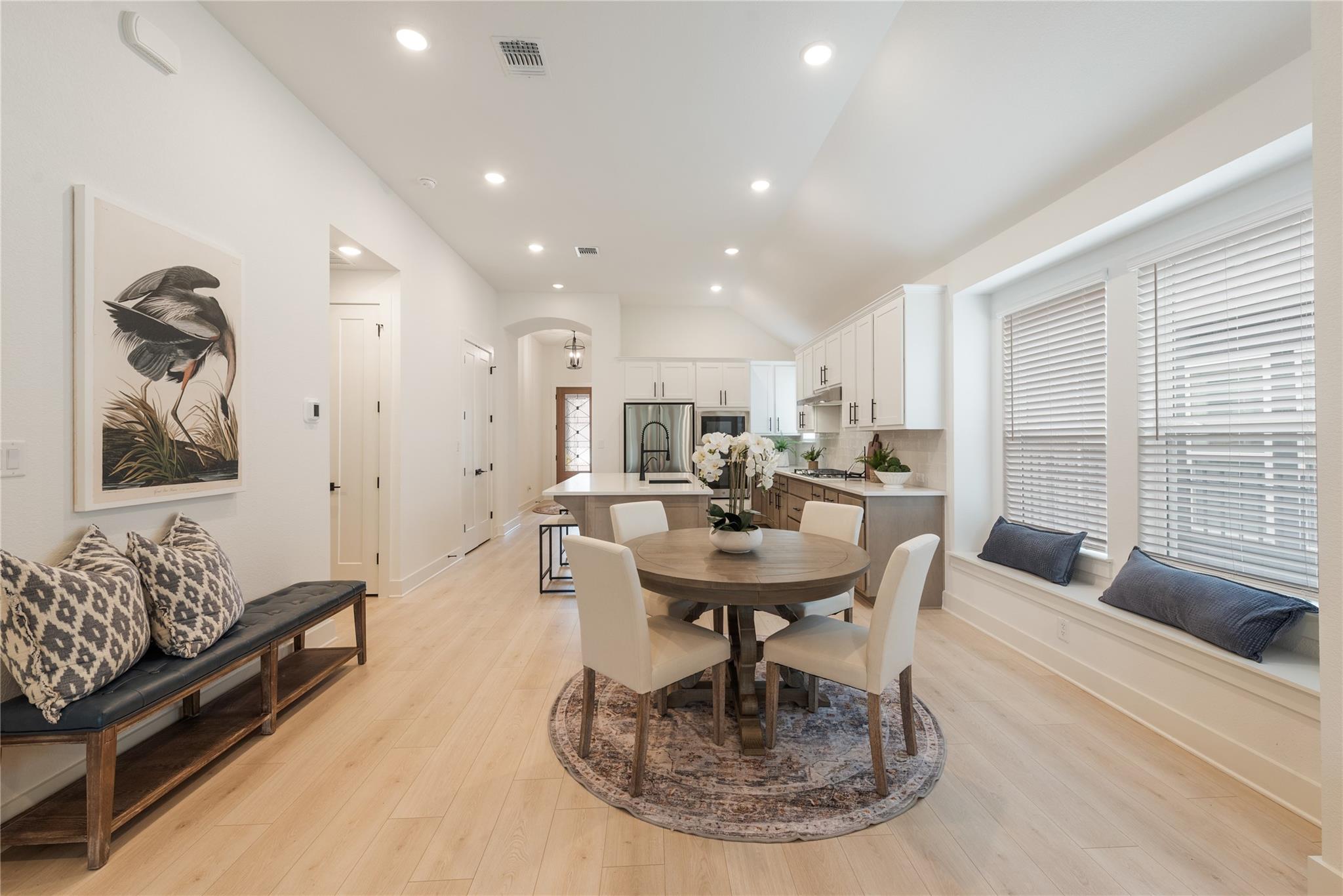 Open-plan kitchen and dining area with a round table, window bench, and white cabinetry.