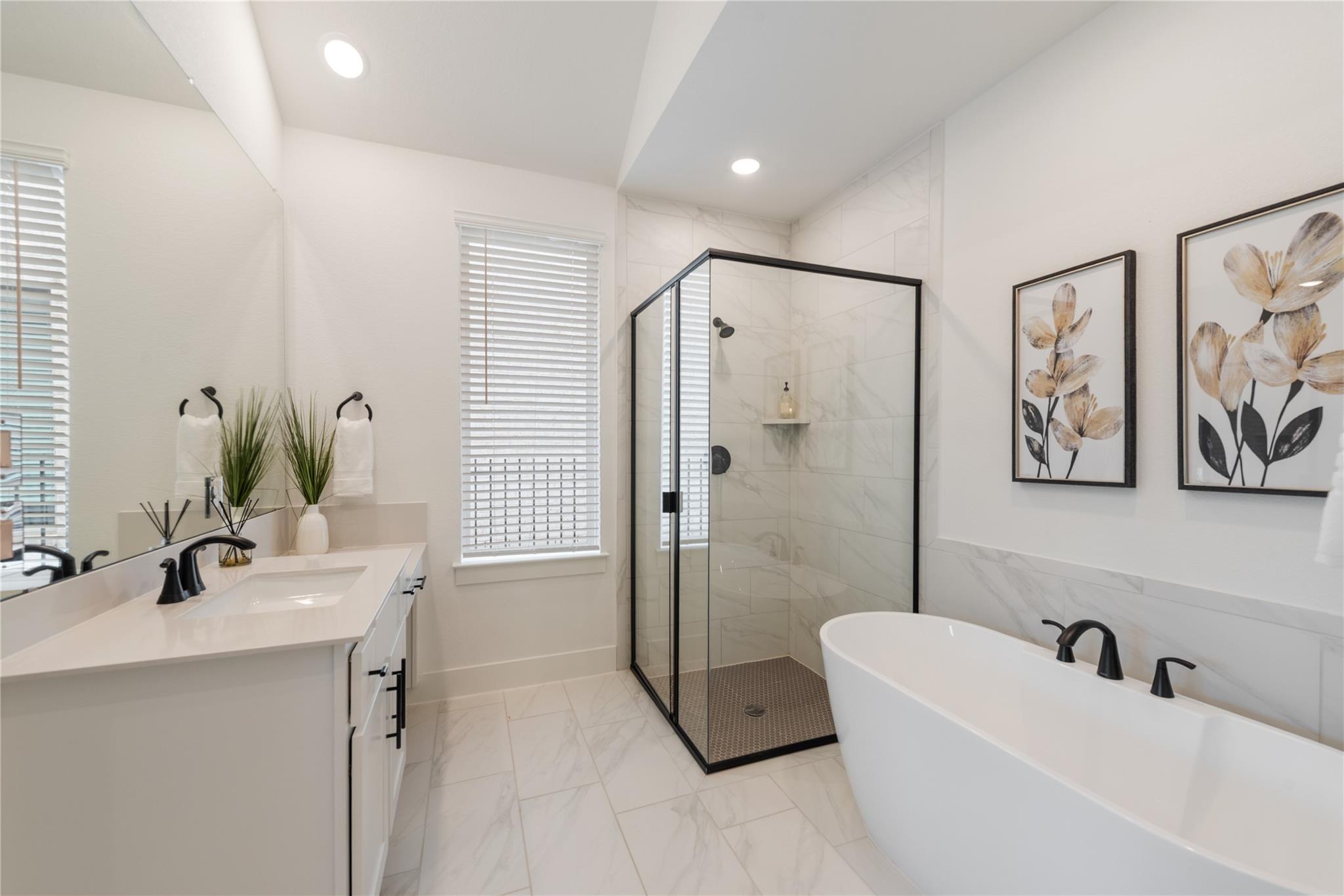 Bright bathroom with a glass-enclosed shower, freestanding tub, and white marble-look tile.