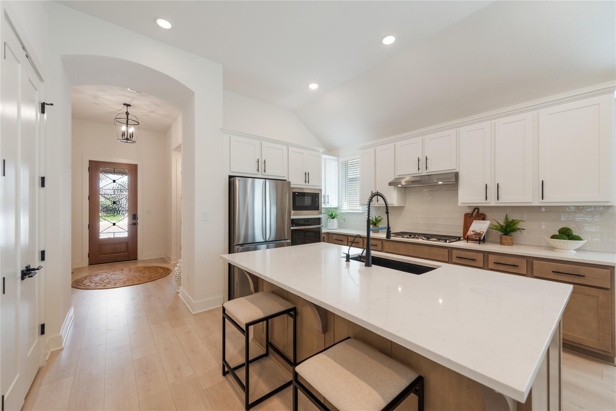 Bright kitchen with a large island, white cabinetry, stainless appliances, and a view toward the front entry.