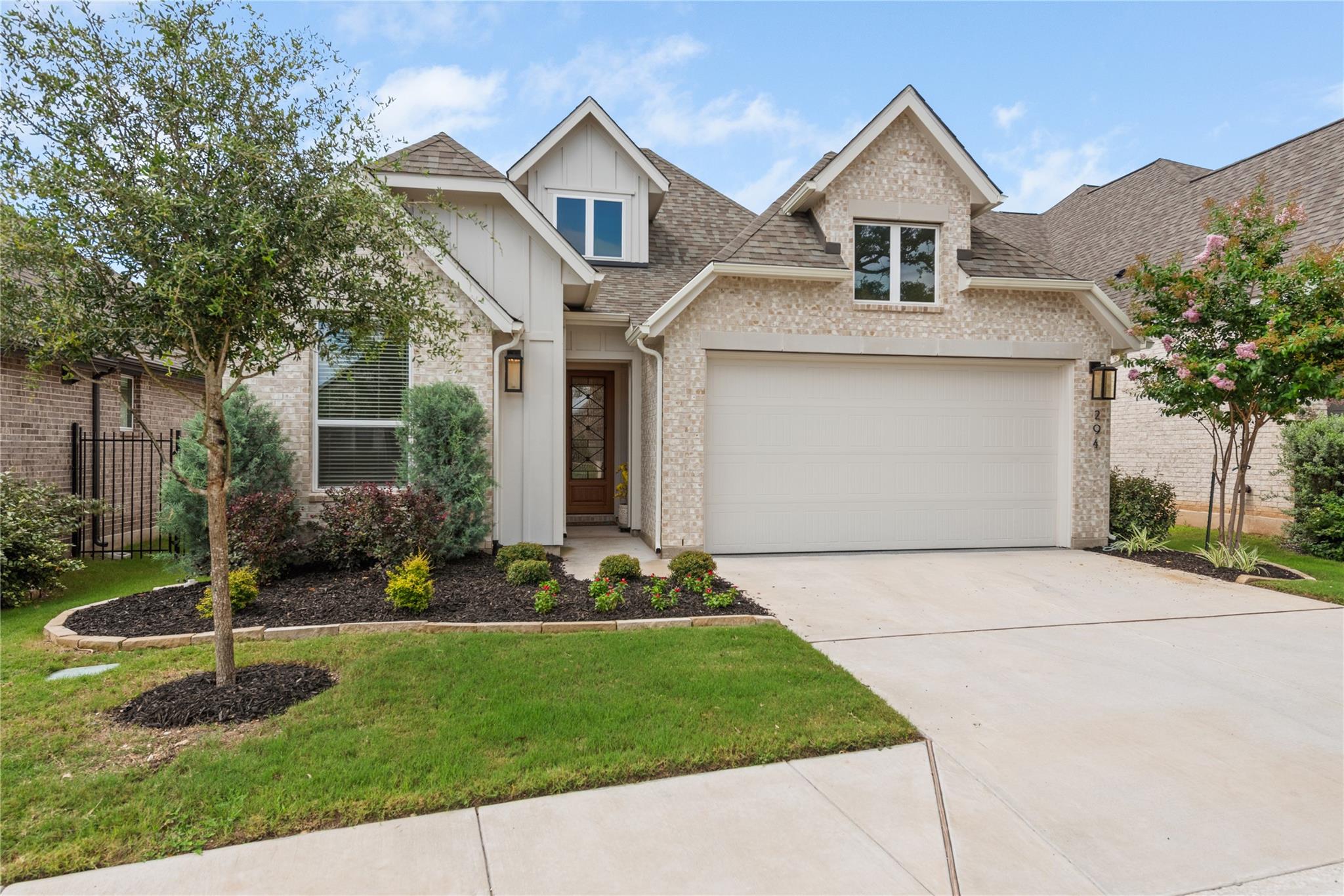 Two-story brick home with a white double garage, landscaped beds, and a covered entry.