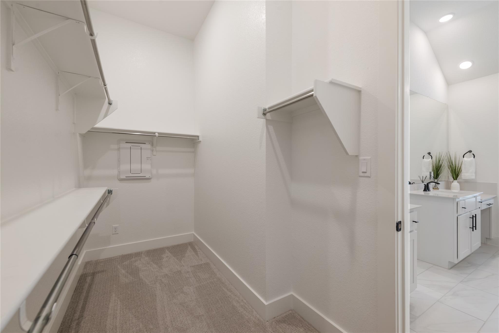 Walk-in closet with carpeted floor, multiple storage rods and shelves, opening to a bathroom vanity.