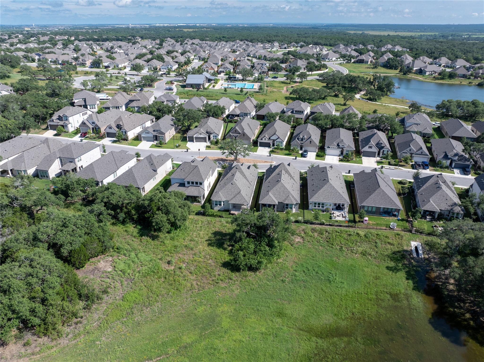 Aerial view of a residential neighborhood beside a pond and broad greenbelt.