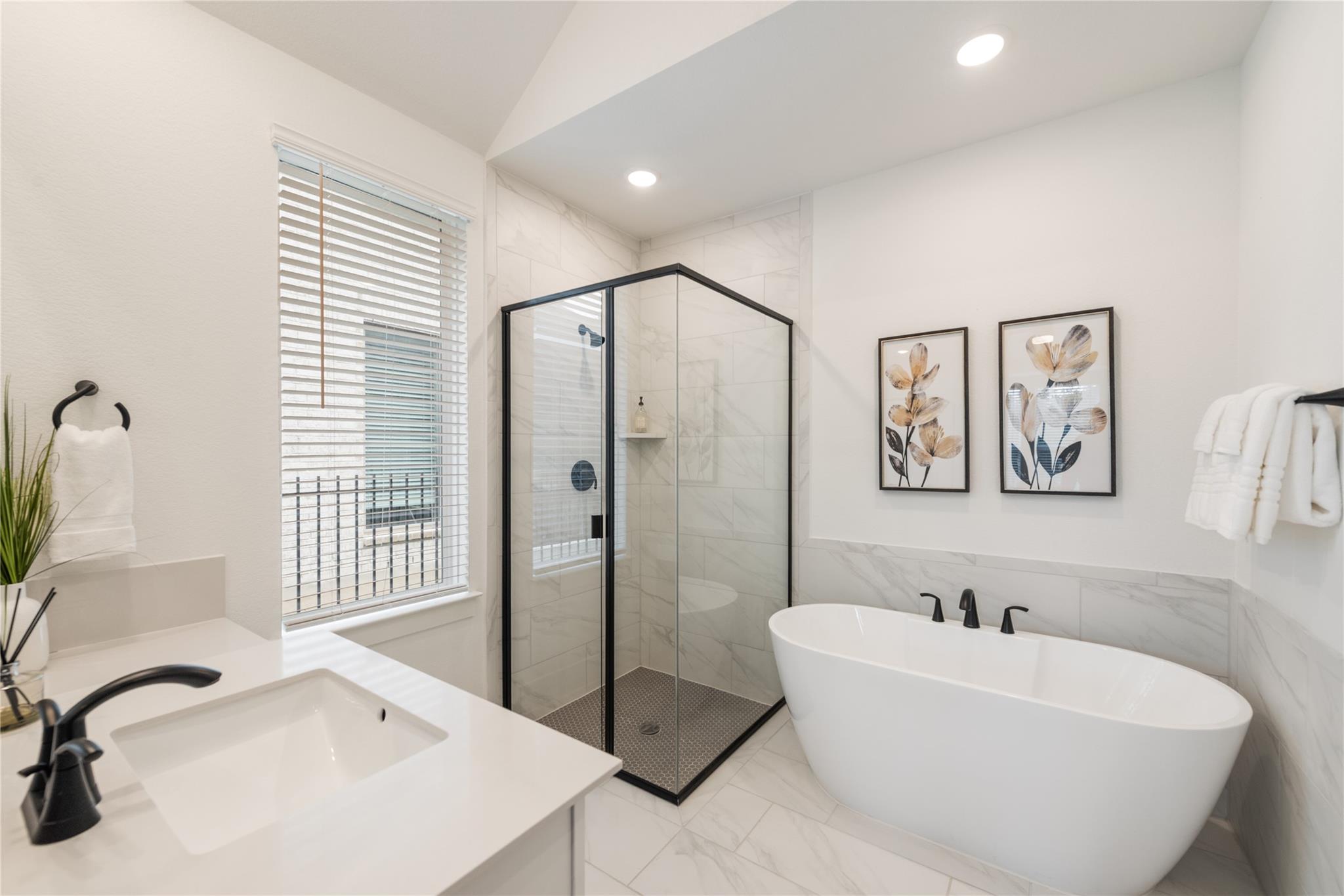 Bright bathroom with a glass shower, freestanding tub, and marble-look tile.