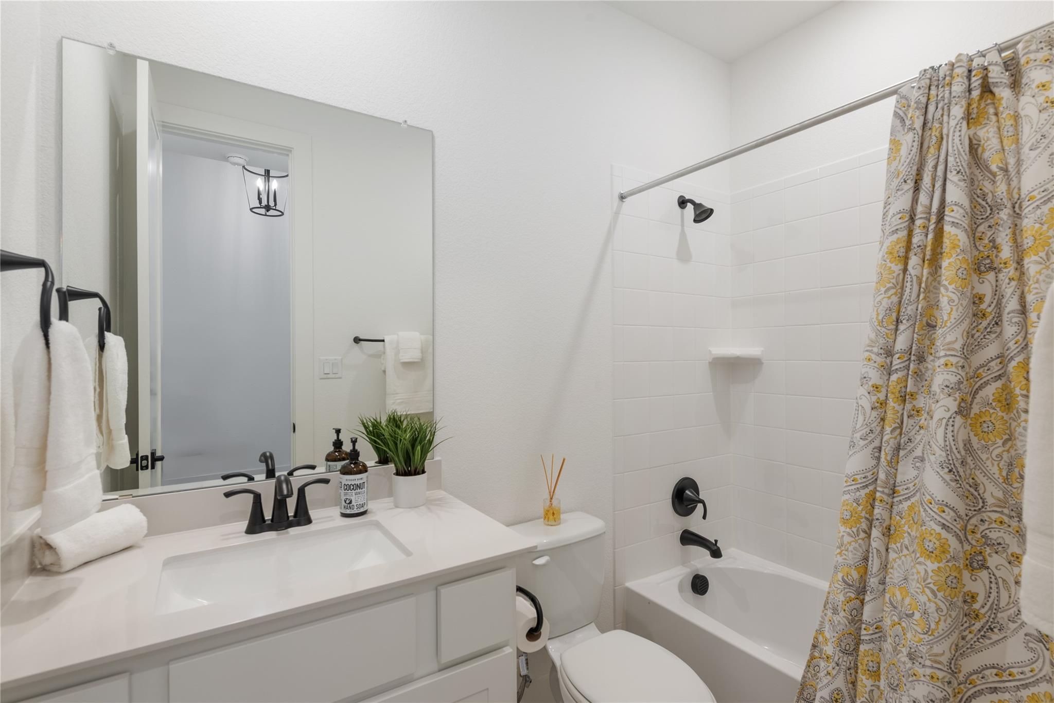 Bathroom with a white vanity, bathtub, black fixtures, and a patterned shower curtain.