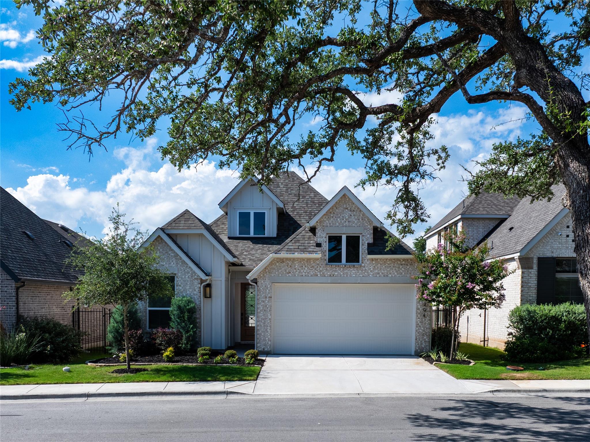 Two-story brick-and-stone home with a white garage, framed by a large oak tree.