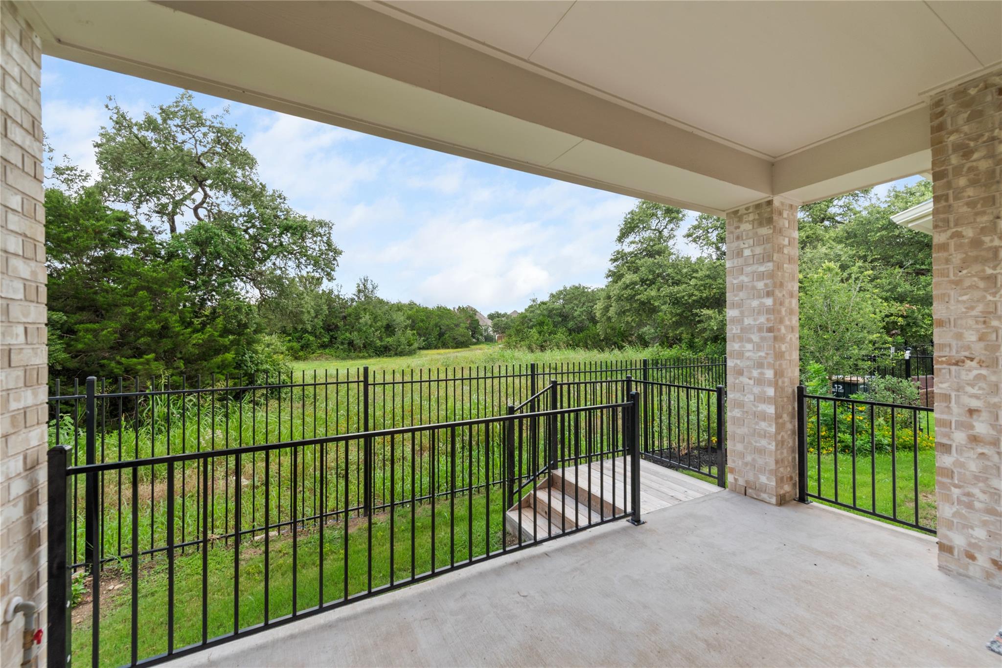 Covered patio with black metal railings overlooking a grassy, tree-lined greenbelt.